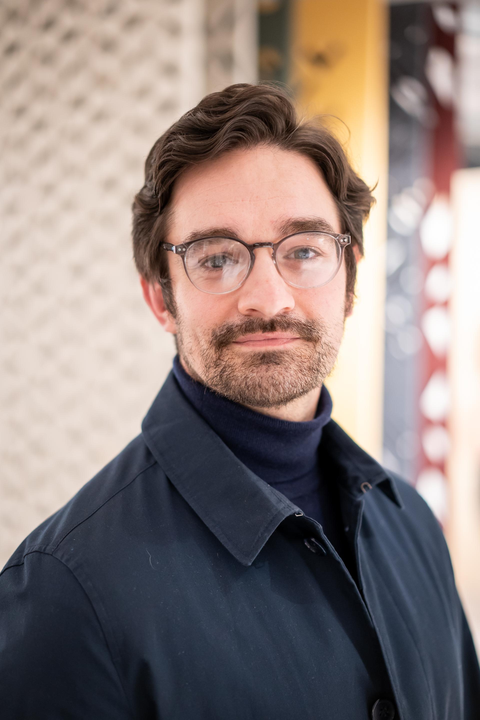 Young man with glasses and a navy coat, conveying themes of sustainability and environmental responsibility.