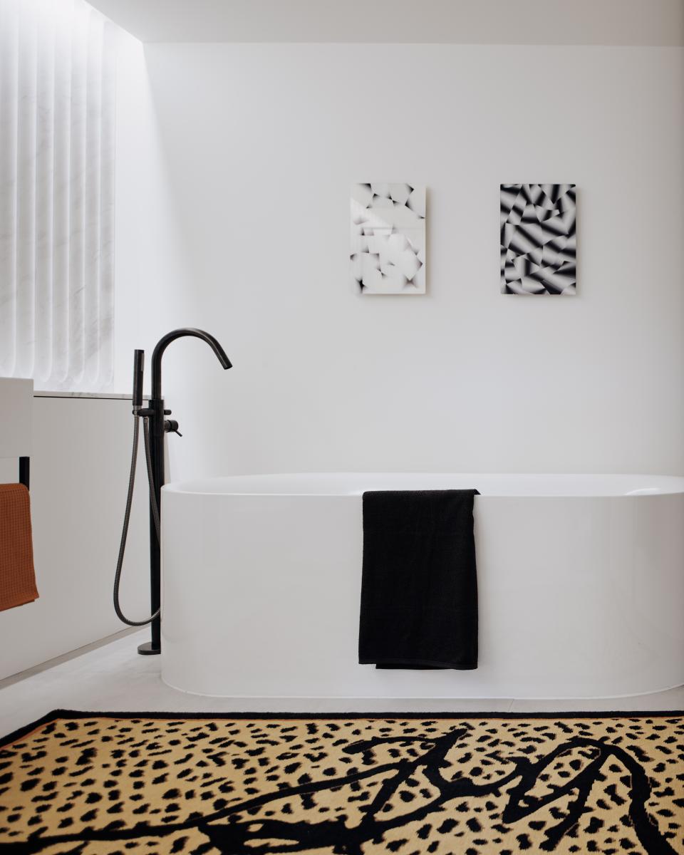Elegant bathroom featuring a freestanding white tub, stylish black towel, and modern art, designed by Bella Freud and Maria Speake.