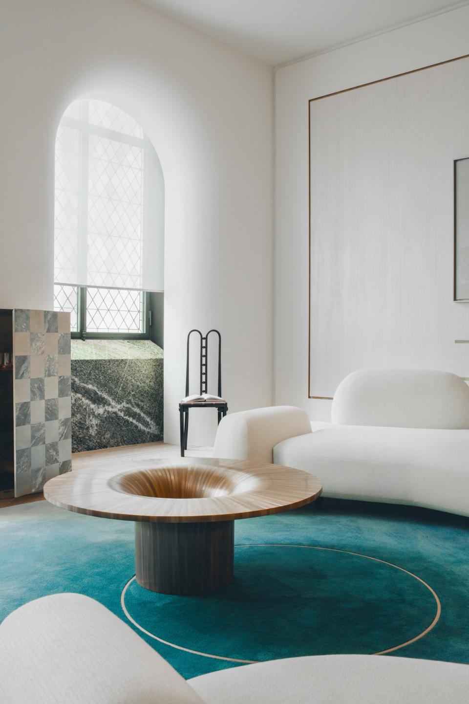 Mathieu Lehanneur's contemporary living room features a unique wooden coffee table, plush seating, and a striking turquoise rug.