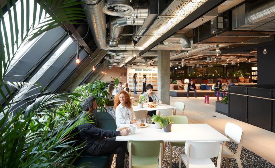 Modern workspace interior featuring employees engaging in conversations and collaboration among greenery and contemporary furnishings.