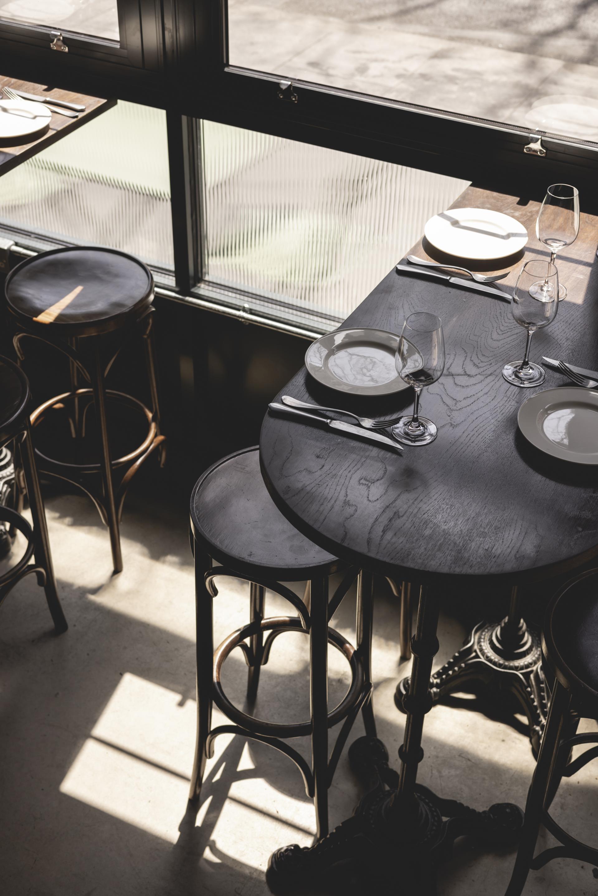Stylish black wooden table set with plates and wine glasses in Bottle + Rye, a Parisian-inspired wine bar and bistro.