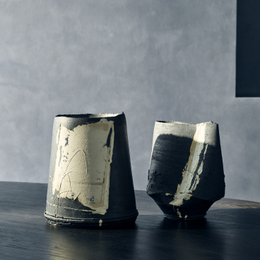 Artistic ceramic vases displayed on a wooden table, showcasing unique textures and a blend of dark and light colors.