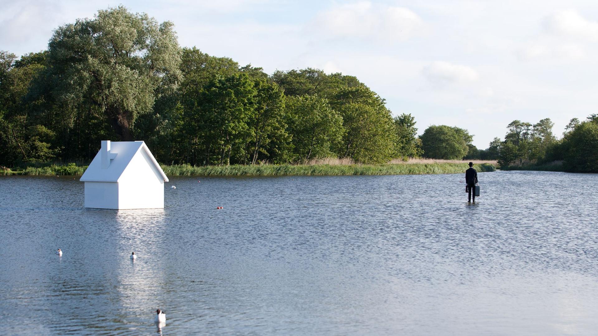 Surreal scene of a floating white house on water, with a figure in formal attire standing nearby.