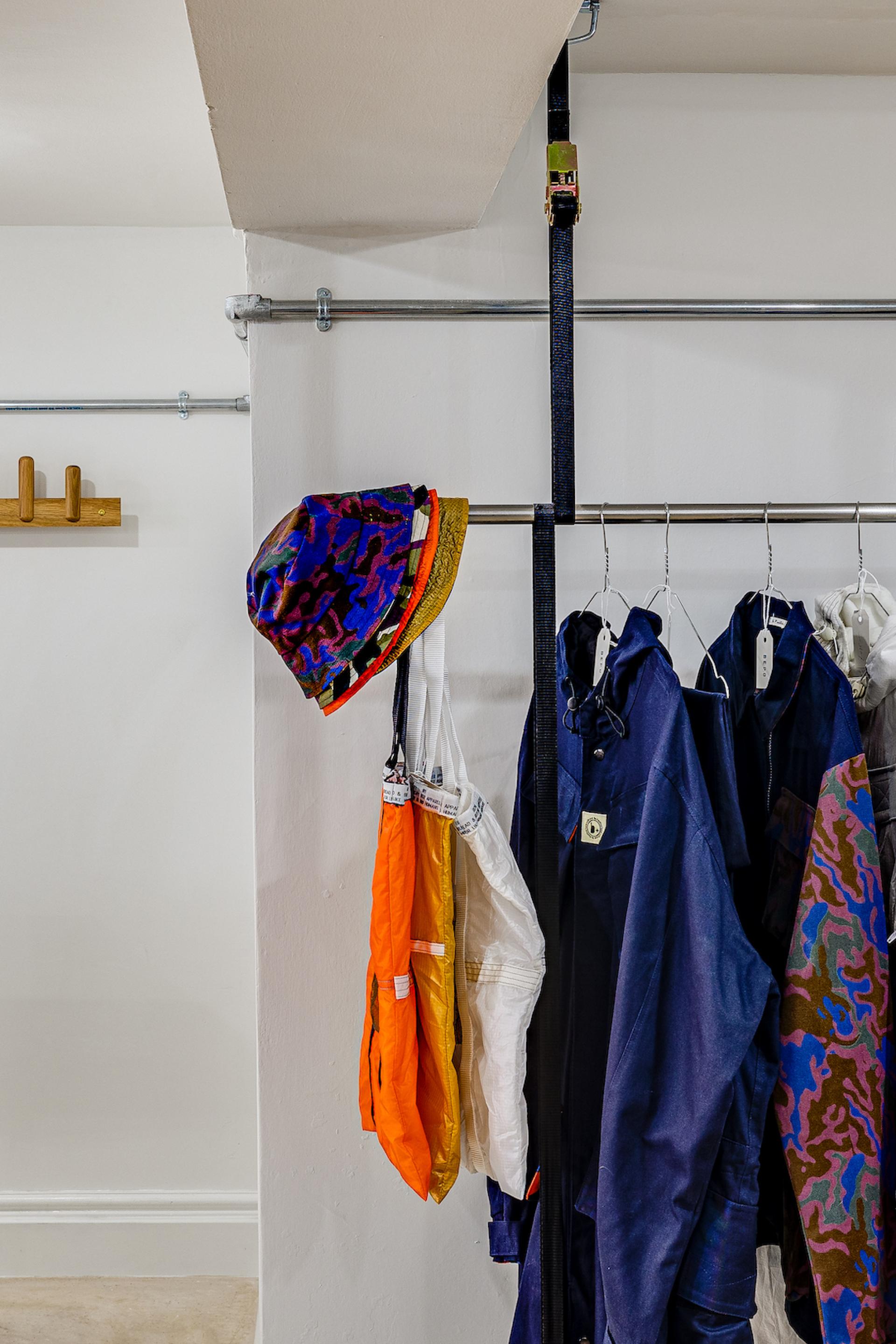Colorful hats and garments displayed on a modern clothing rack in a stylish interior design space by MONIKA Studio.