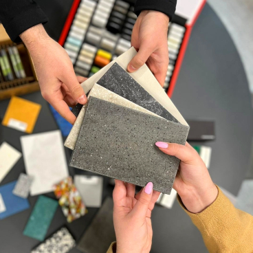 Hands holding various samples of solid surface materials, showcasing texture and color options for sustainable design solutions.