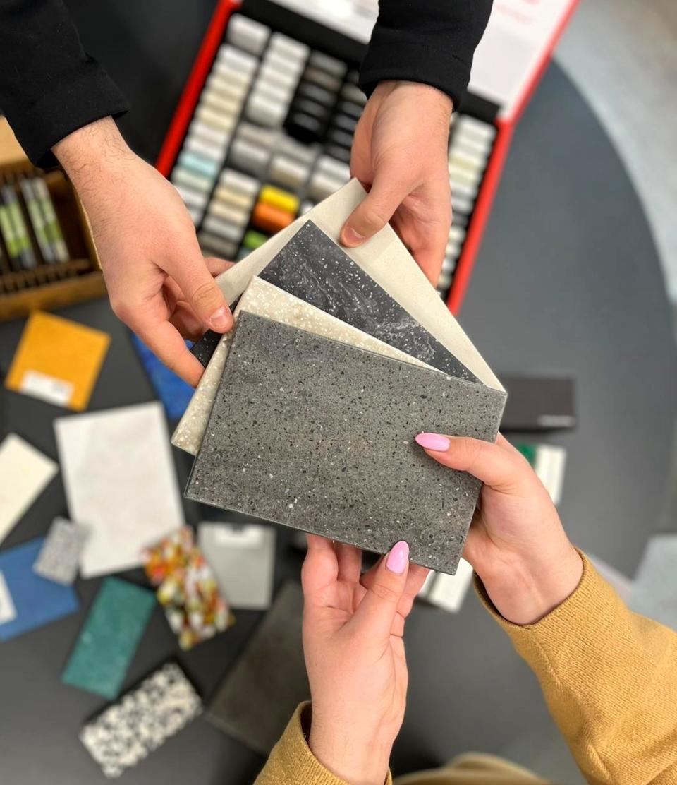 Hands holding various samples of solid surface materials, showcasing texture and color options for sustainable design solutions.
