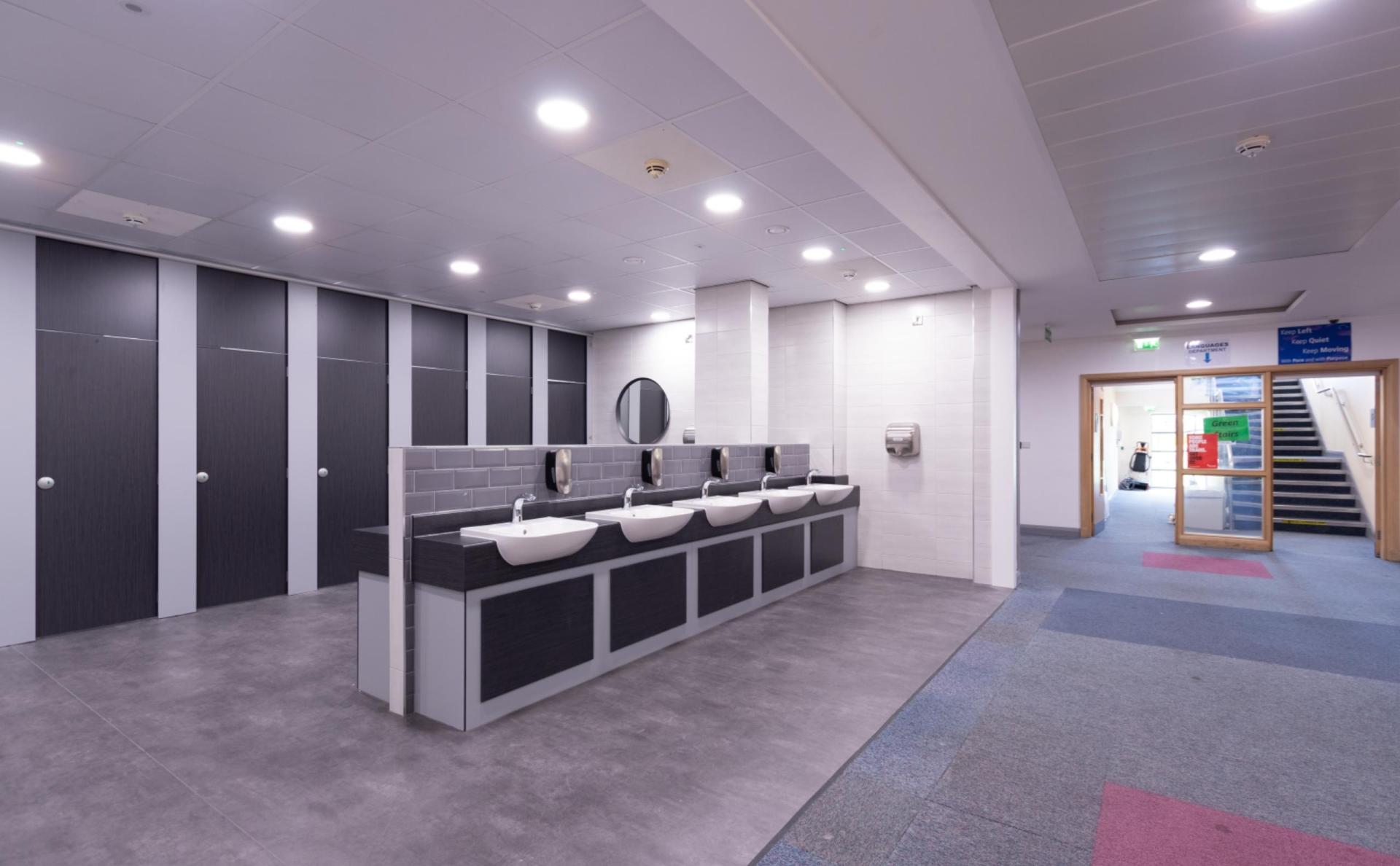 Modern gender neutral washroom featuring multiple sinks, privacy stalls, and accessible design elements for educational spaces.