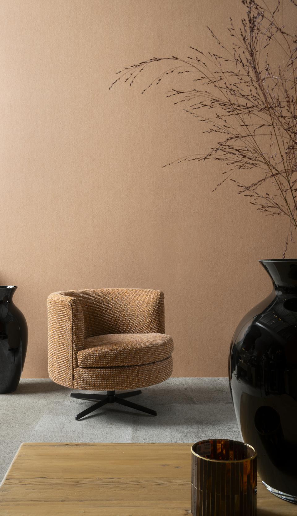 Stylish interior featuring a round, textured armchair against a warm-toned wall, complemented by elegant vases and decor elements.