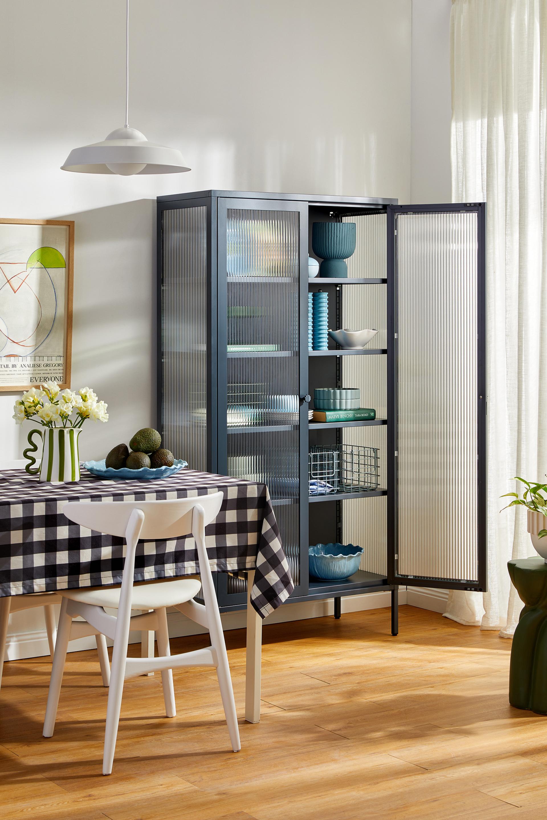 Stylish modern cabinet from Mustard Made's Glass Collection, featuring various dishware against a cozy dining setting.