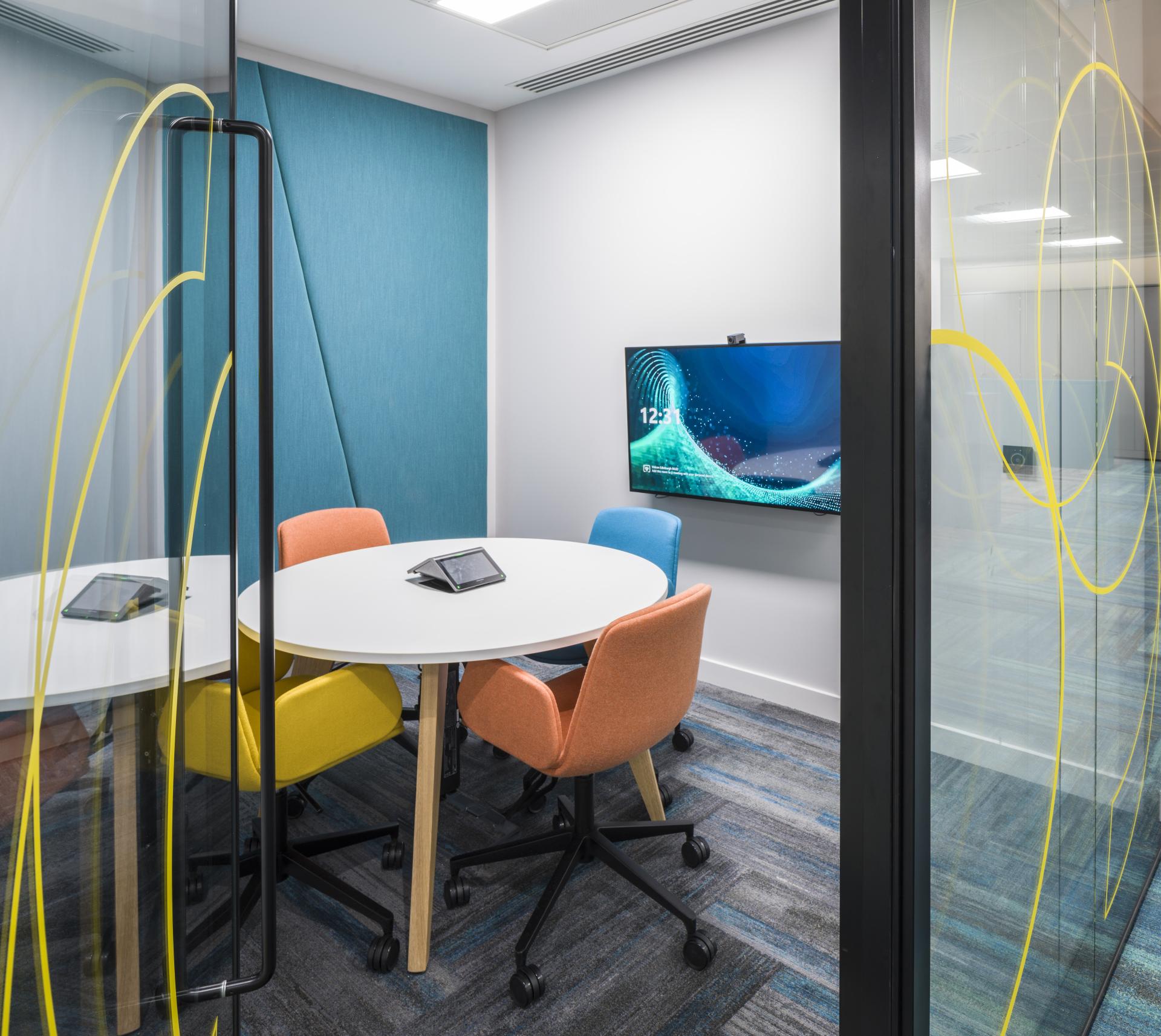 Modern conference room featuring a round table, colorful chairs, and a screen, part of Scotland's first WELL certified office.