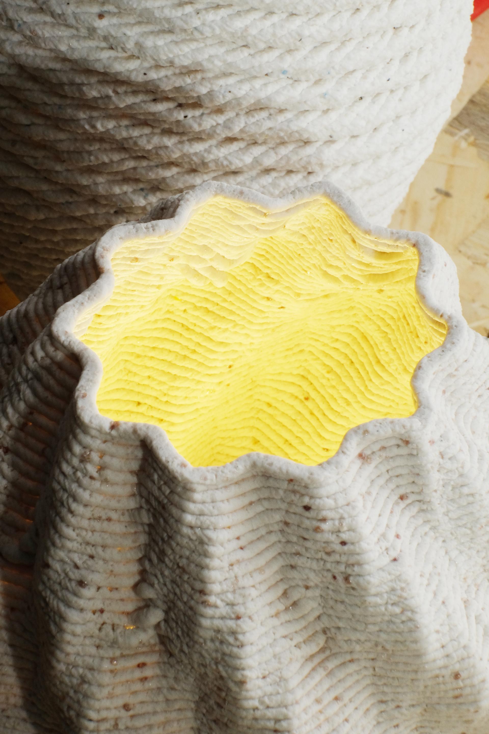 3D printed ceramic lamp with a textured exterior, emitting a warm yellow glow, showcasing sustainable design principles.