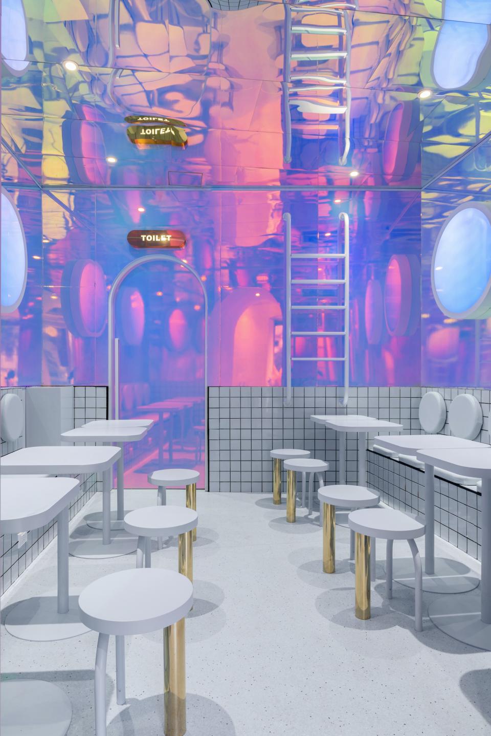 Interior of Masquespacio's Bun restaurant in Milan featuring modern design, white tables, and vibrant reflective walls.