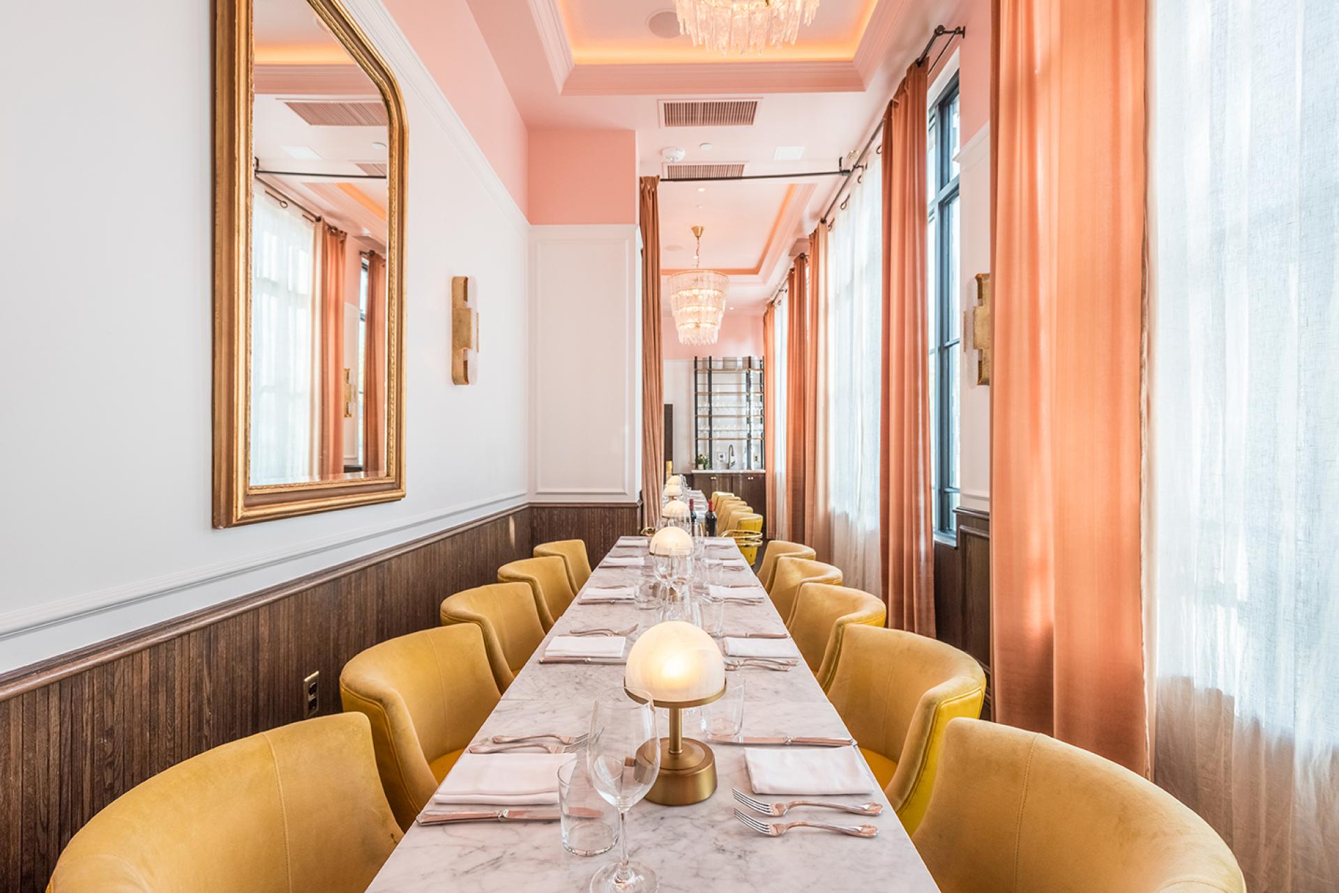 Bright, elegant dining area of The Draycott, featuring yellow chairs, marble table, and soft pink drapery.