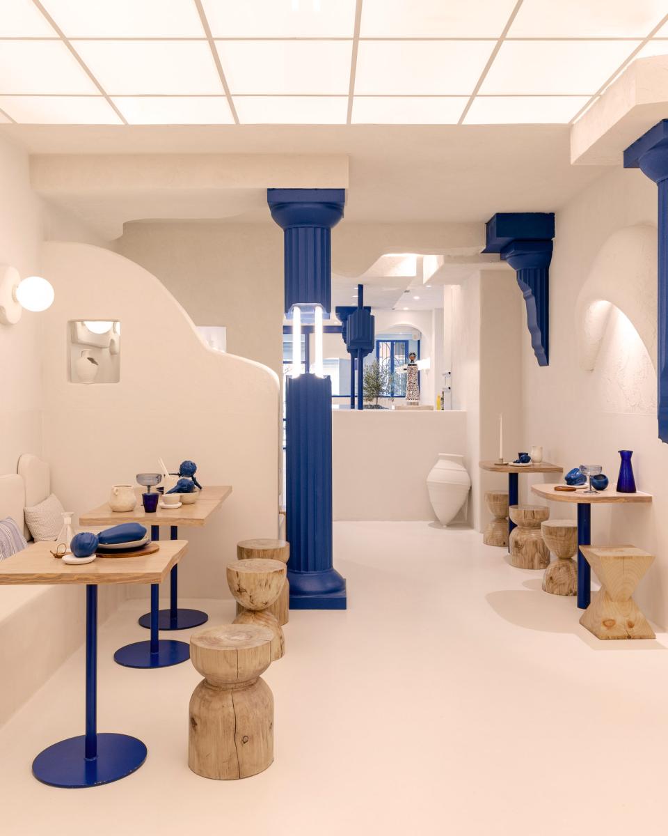 Modern Greek restaurant interior featuring minimalist tables, blue accents, and traditional wooden stools, reflecting Egeo's design ethos.