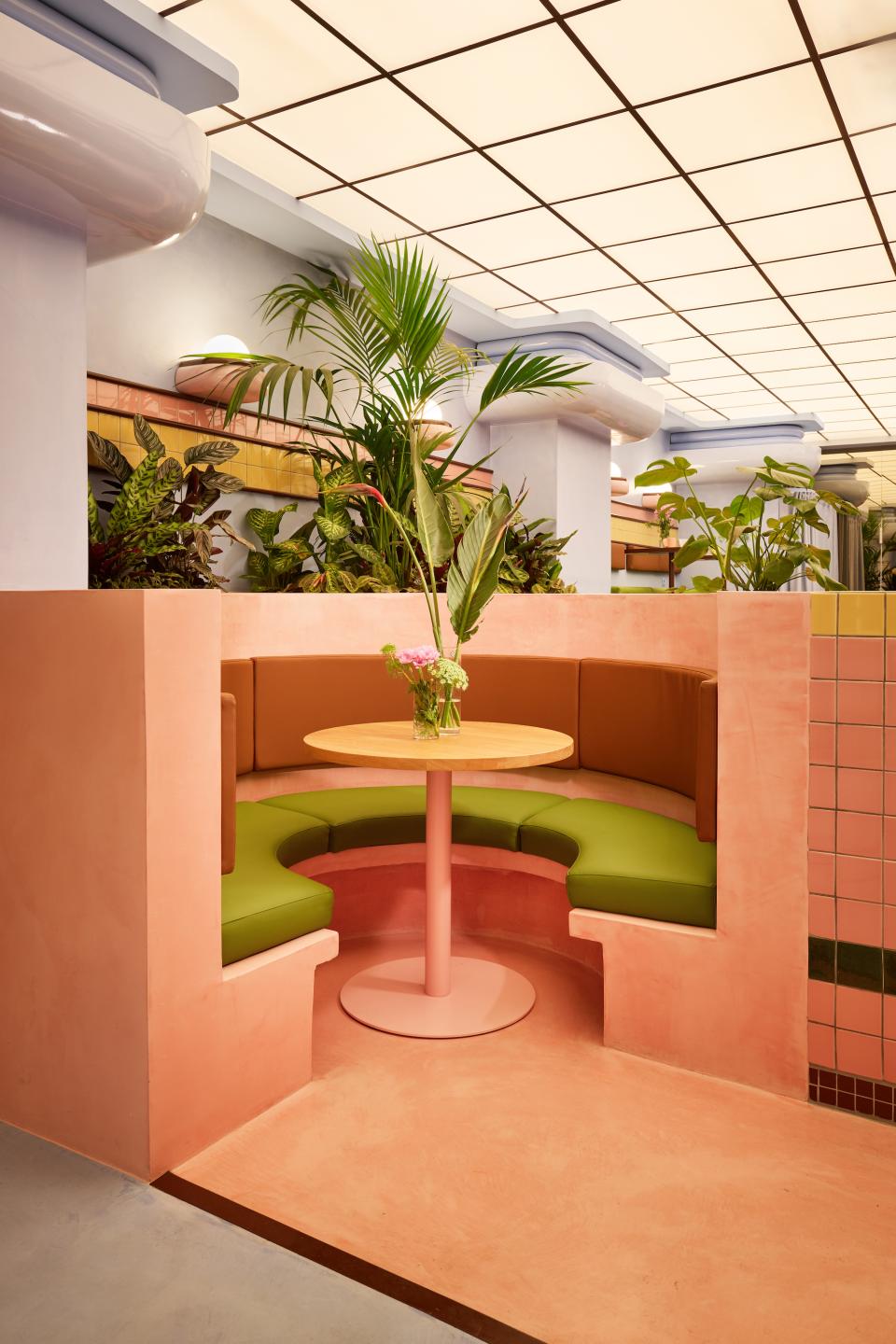 Vibrant Art Deco-inspired seating nook with tropical plants, showcasing a pink and green color palette in a Barcelona ice cream parlor.