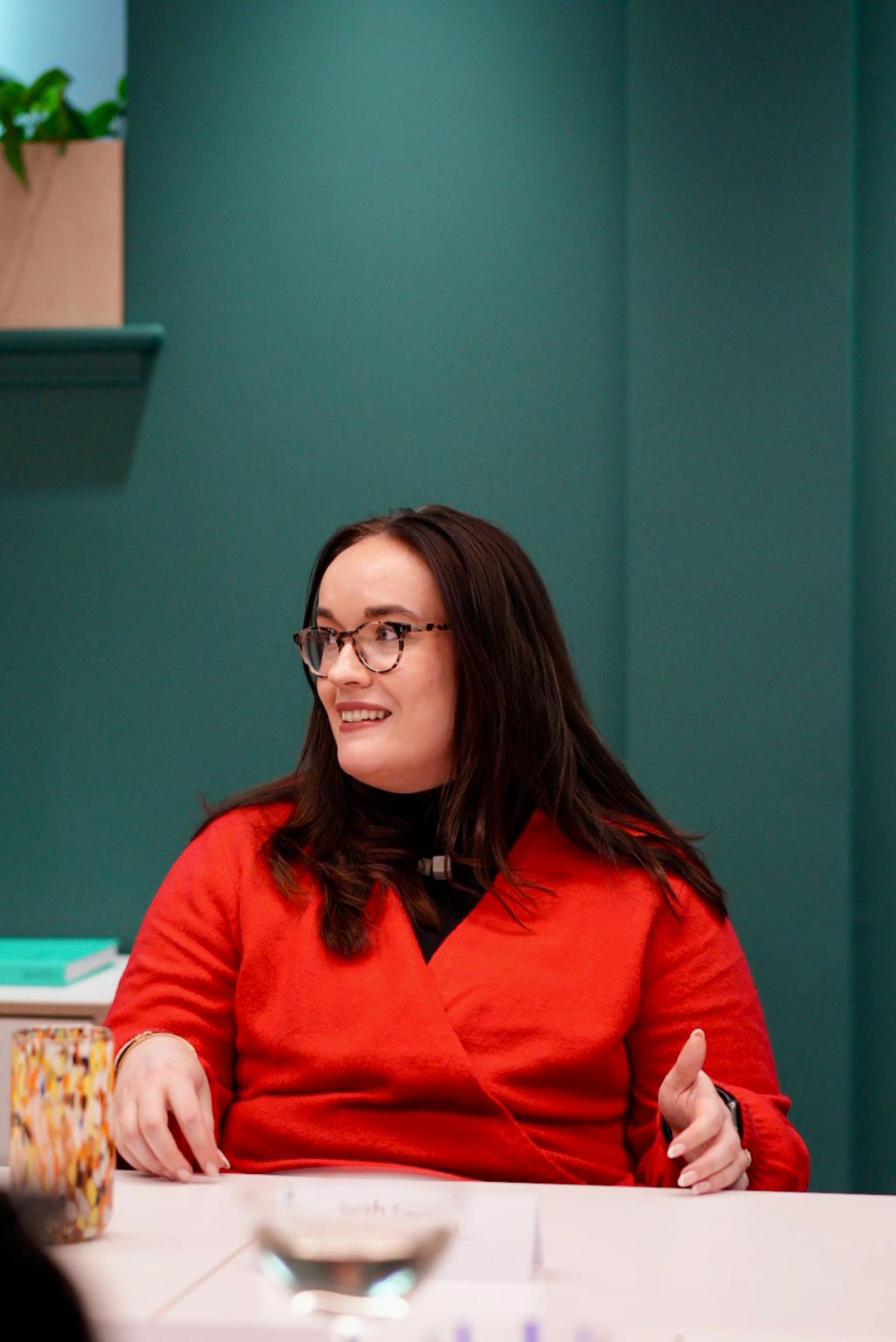 Woman in a red sweater engaged in a discussion about workplace flexibility, set against a teal background.