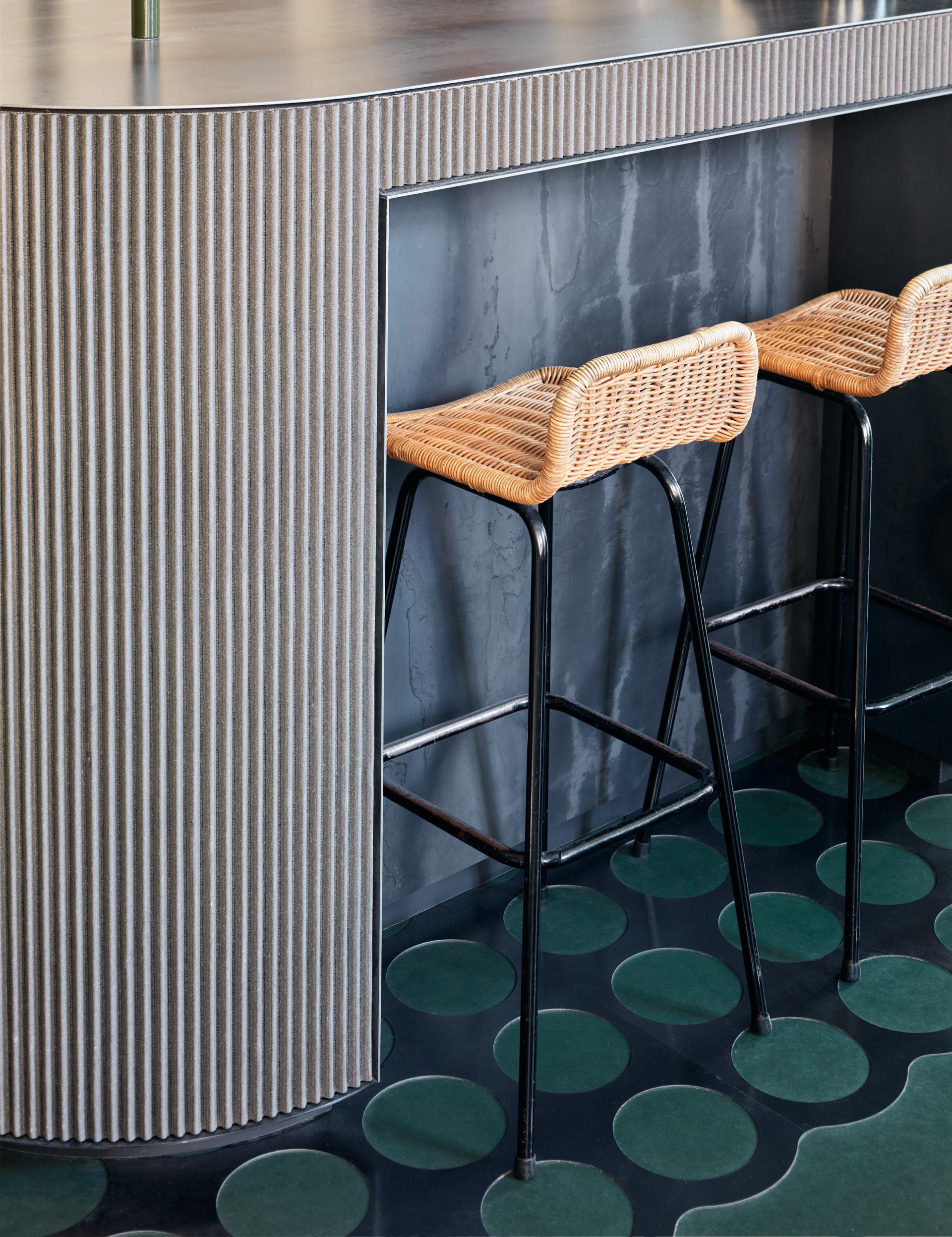 Modern bar design featuring textured gray counter and woven stools in the COEF clothing shop.