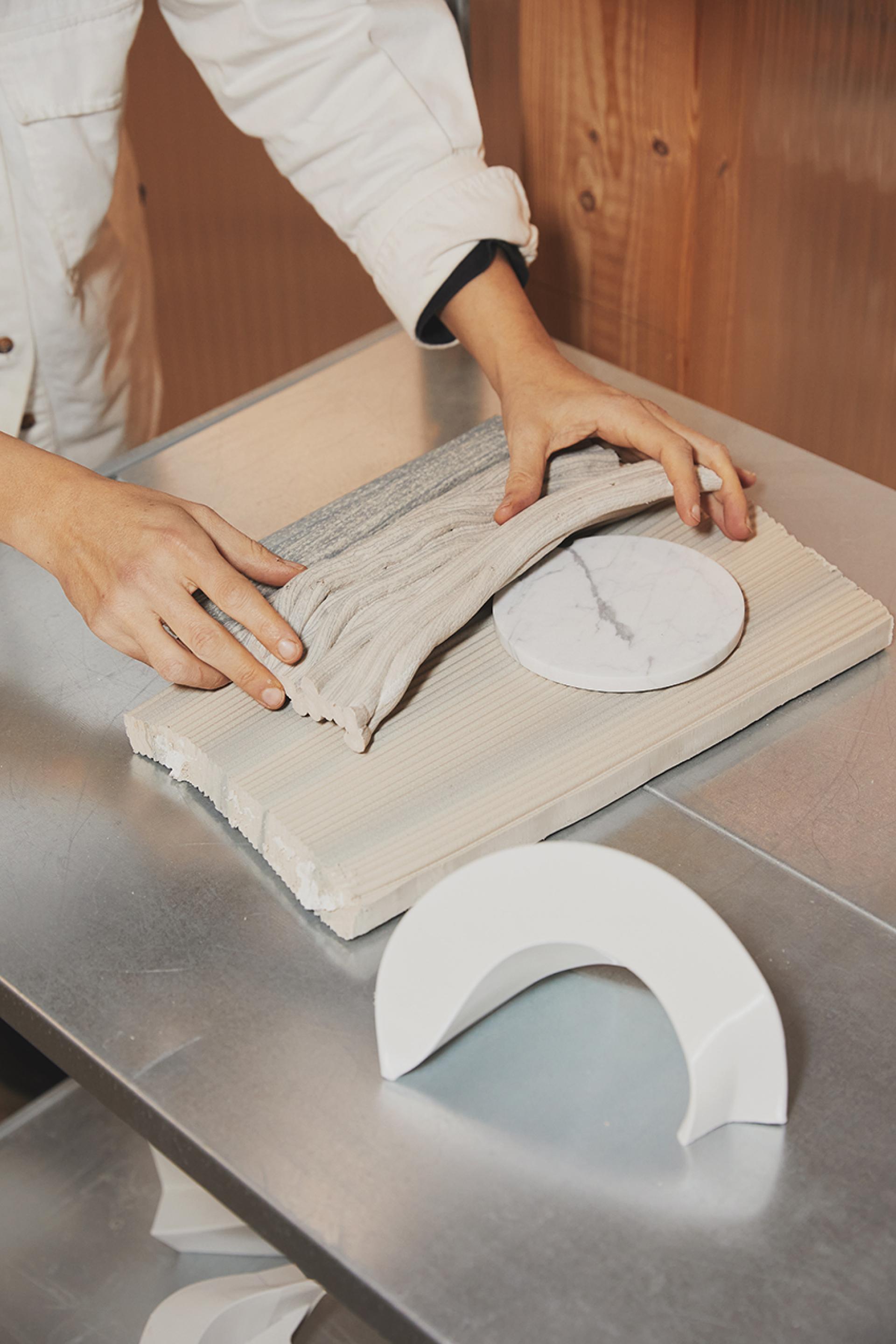 Hands molding various materials on a table, showcasing the design process for The New Raw's Stratum furniture.