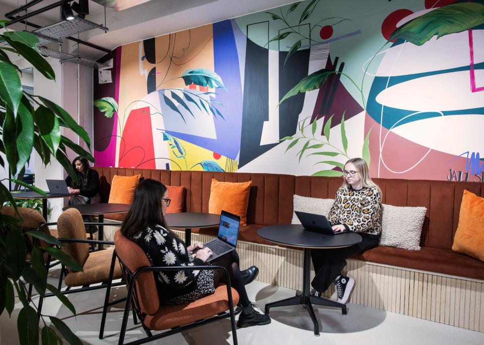 Vibrant workspace featuring colorful mural, cozy seating, and people working on laptops at Runway East.