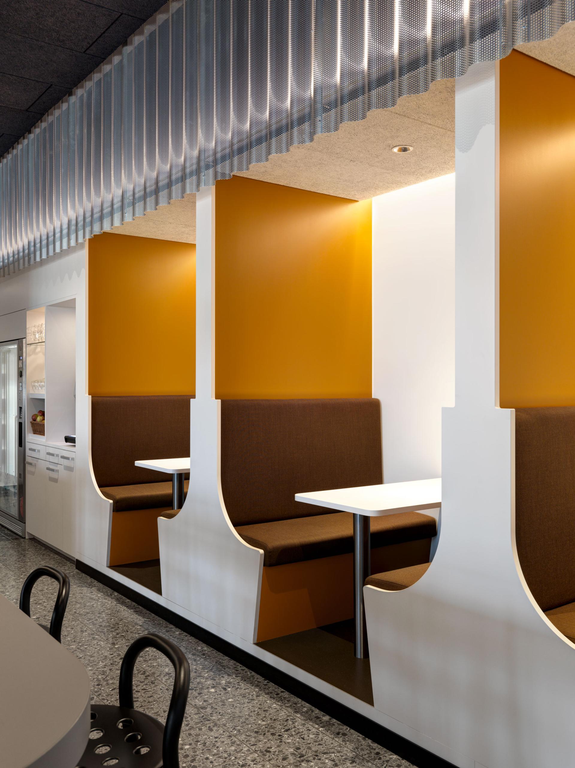 Modern seating area with brown booths and vibrant orange walls, designed by Studio Gessaga for Ferrum AG spaces.