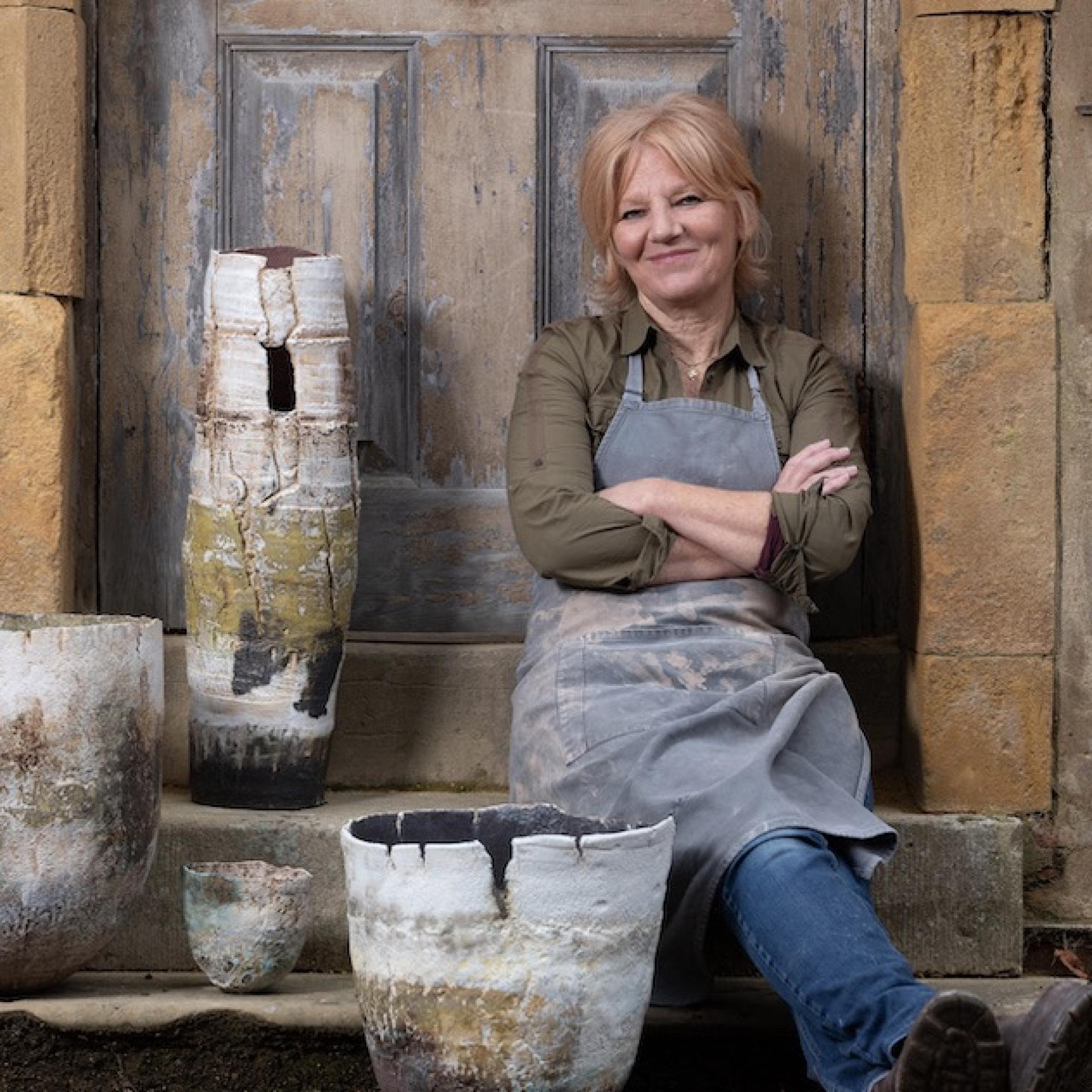 A smiling potter sits beside her handcrafted ceramic pots, showcasing the vibrant creativity of Nottingham's craft community.