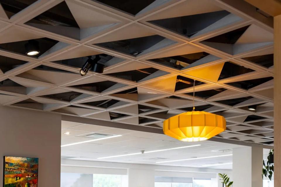 Sculptural acoustic ceiling tiles with a geometric design and yellow pendant light in a modern interior space.