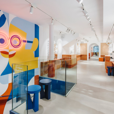 Brightly colored interior of ACE & TATE Barcelona, featuring decorative wall art and stylish eyewear displays.