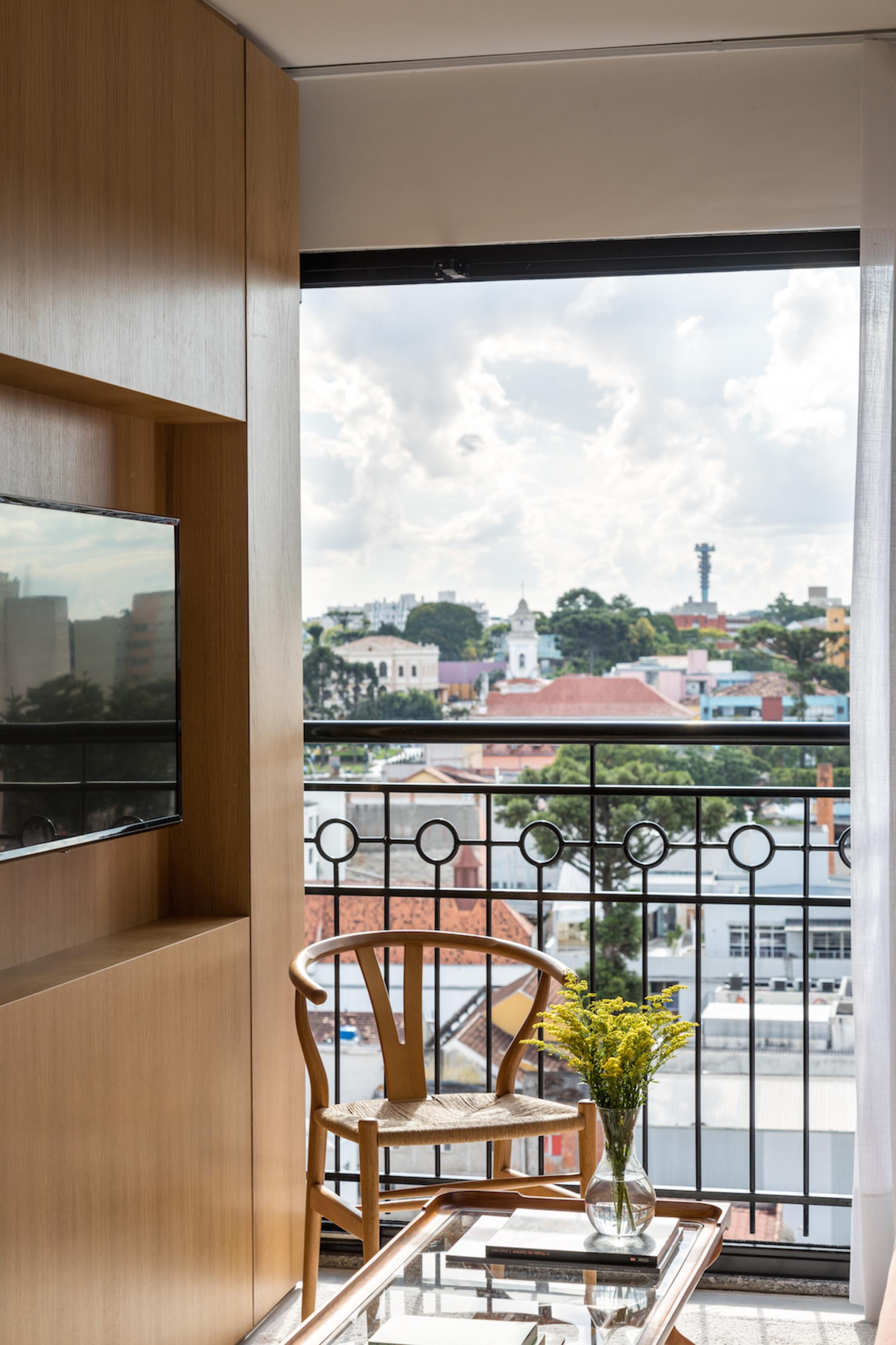 Cozy compact apartment in Curitiba with stylish wooden decor, a view of the city, and a vase of flowers.