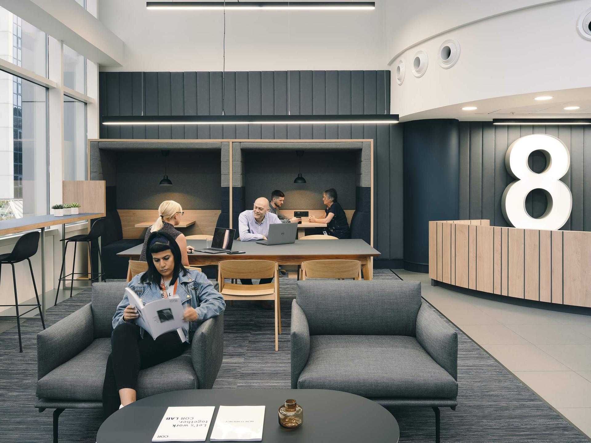 Modern workspace featuring collaborative areas, individuals engaged in design discussions, and a relaxed reading space, emphasizing sustainable design.