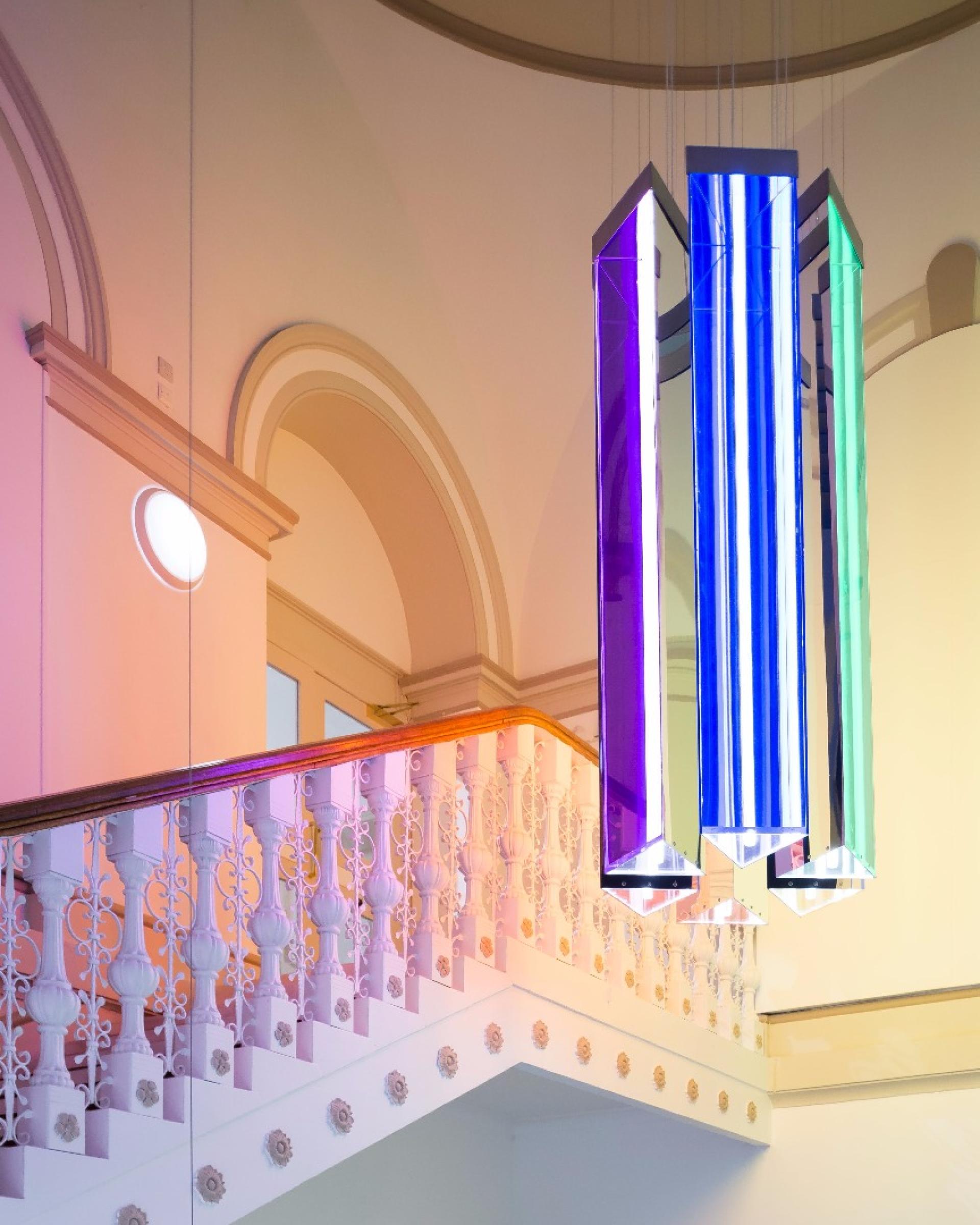 Sustainable interior design featuring vibrant, geometric pendant lights above an elegantly curved staircase with ornate railing.