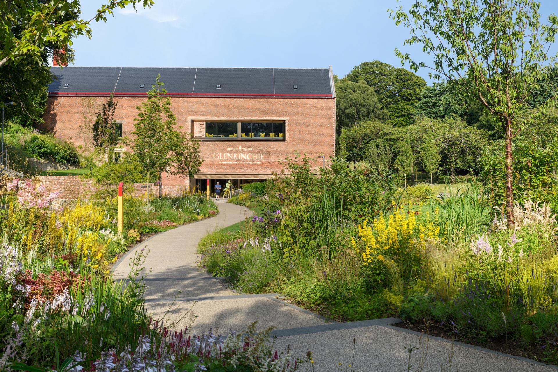 Glenkinchie distillery entrance surrounded by colorful flowers and greenery, showcasing Scotland's architectural beauty and whisky heritage.