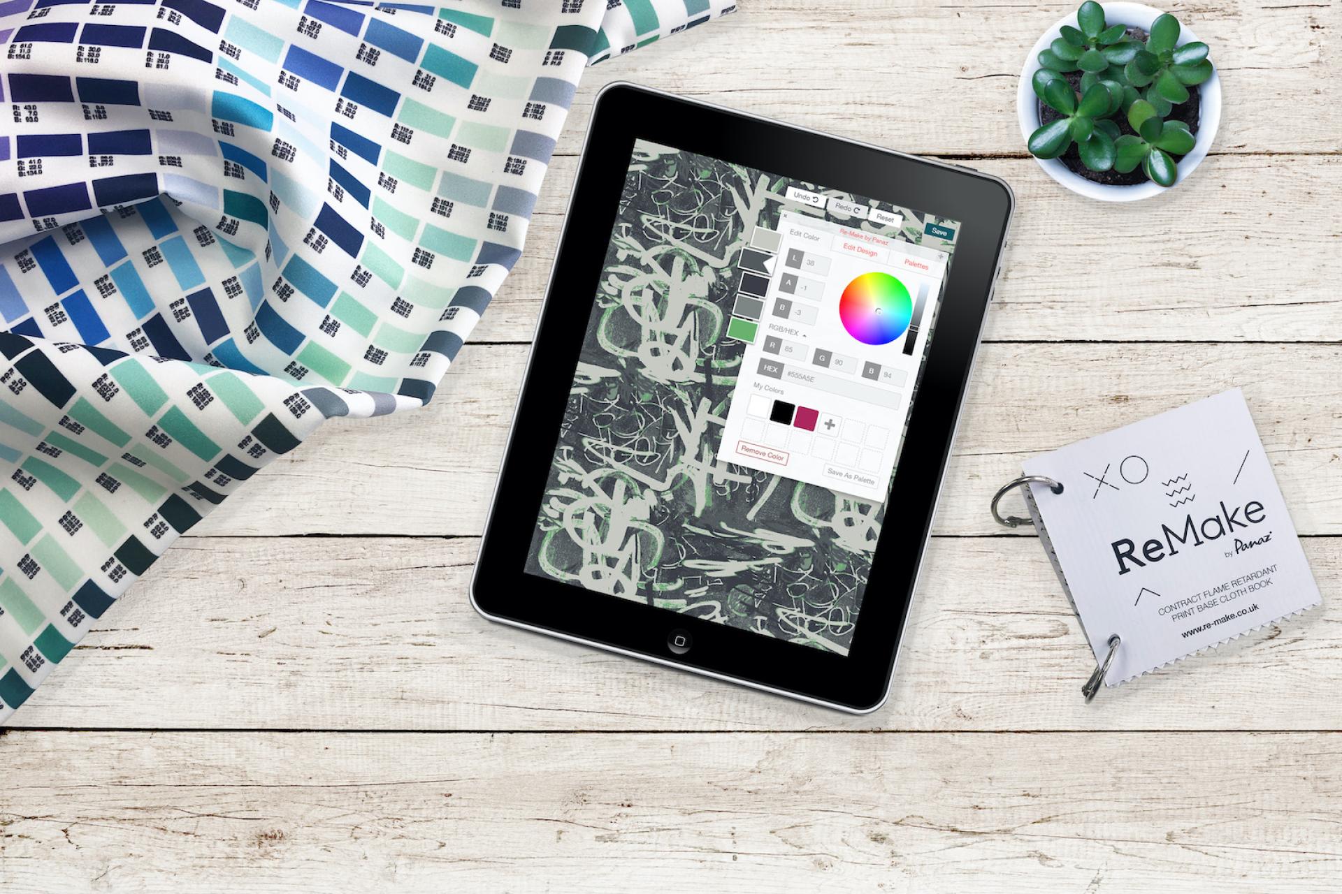 A tablet displaying a fabric design color editing software alongside decorative fabrics and a design inspiration booklet.