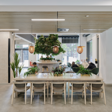 Modern co-working space featuring greenery, a large communal table, and relaxed seating, showcasing Vita Group's uhaus brand design.