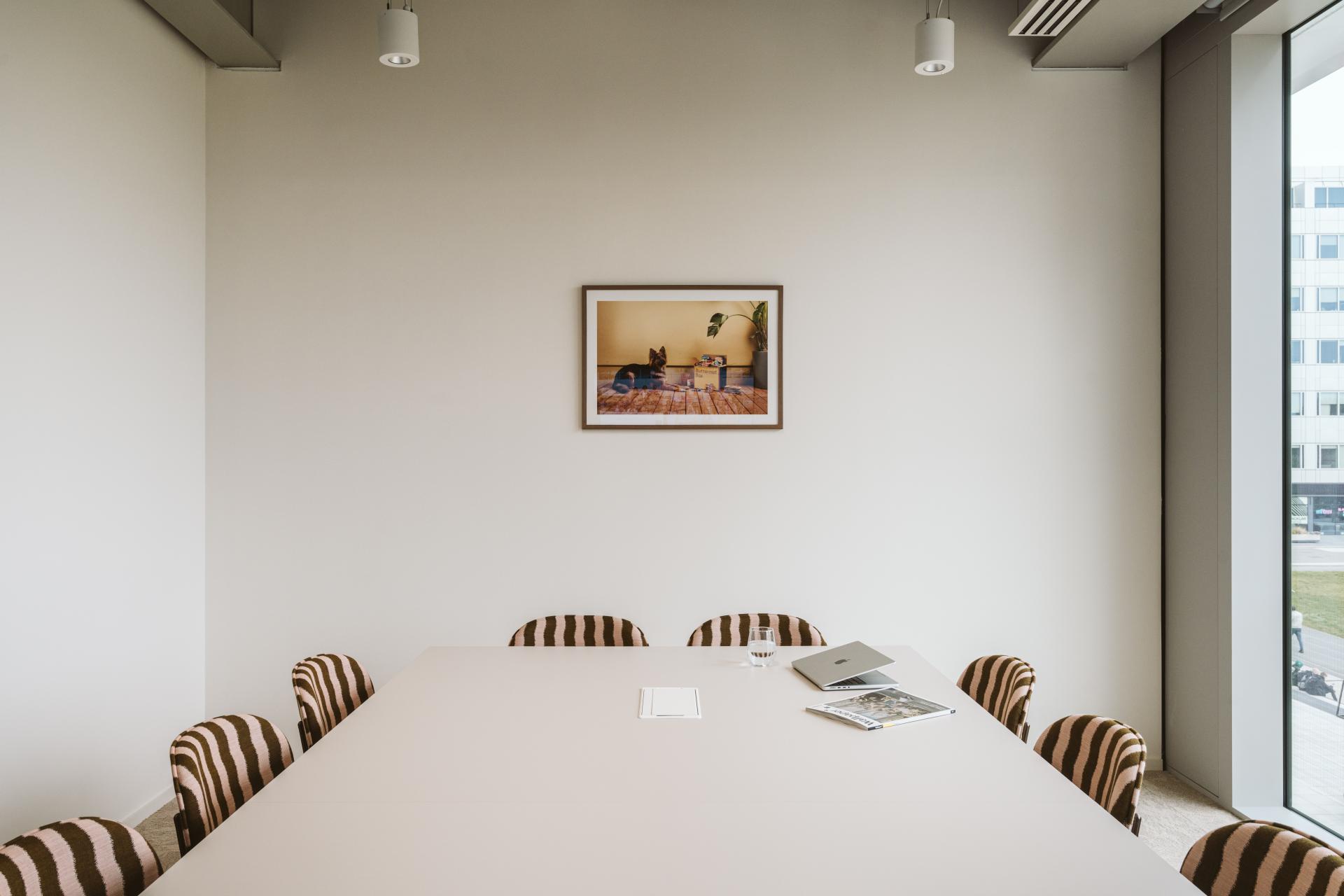 Modern meeting room with striped chairs, a minimalistic table, and a dog-themed artwork enhancing Butternut Box's pet-friendly workspace.