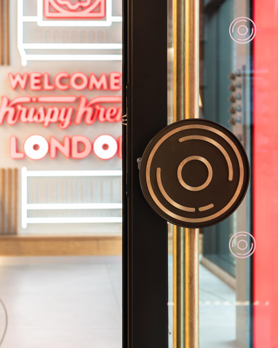 Krispy Kreme's illuminated entrance features a stylish door handle, welcoming visitors to the iconic London store.