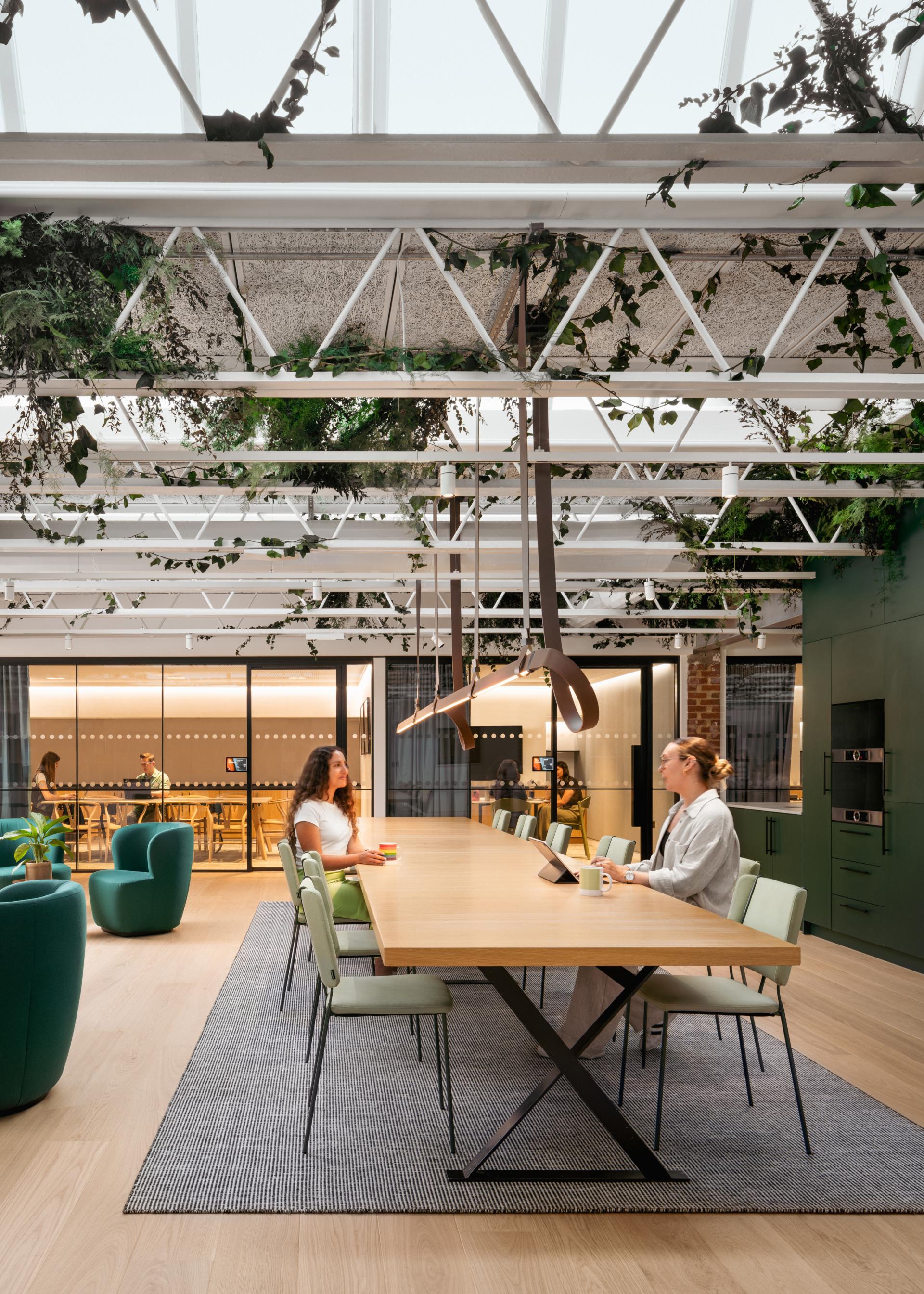 Sustainable office design featuring employees collaborating at a modern table surrounded by greenery and natural light.