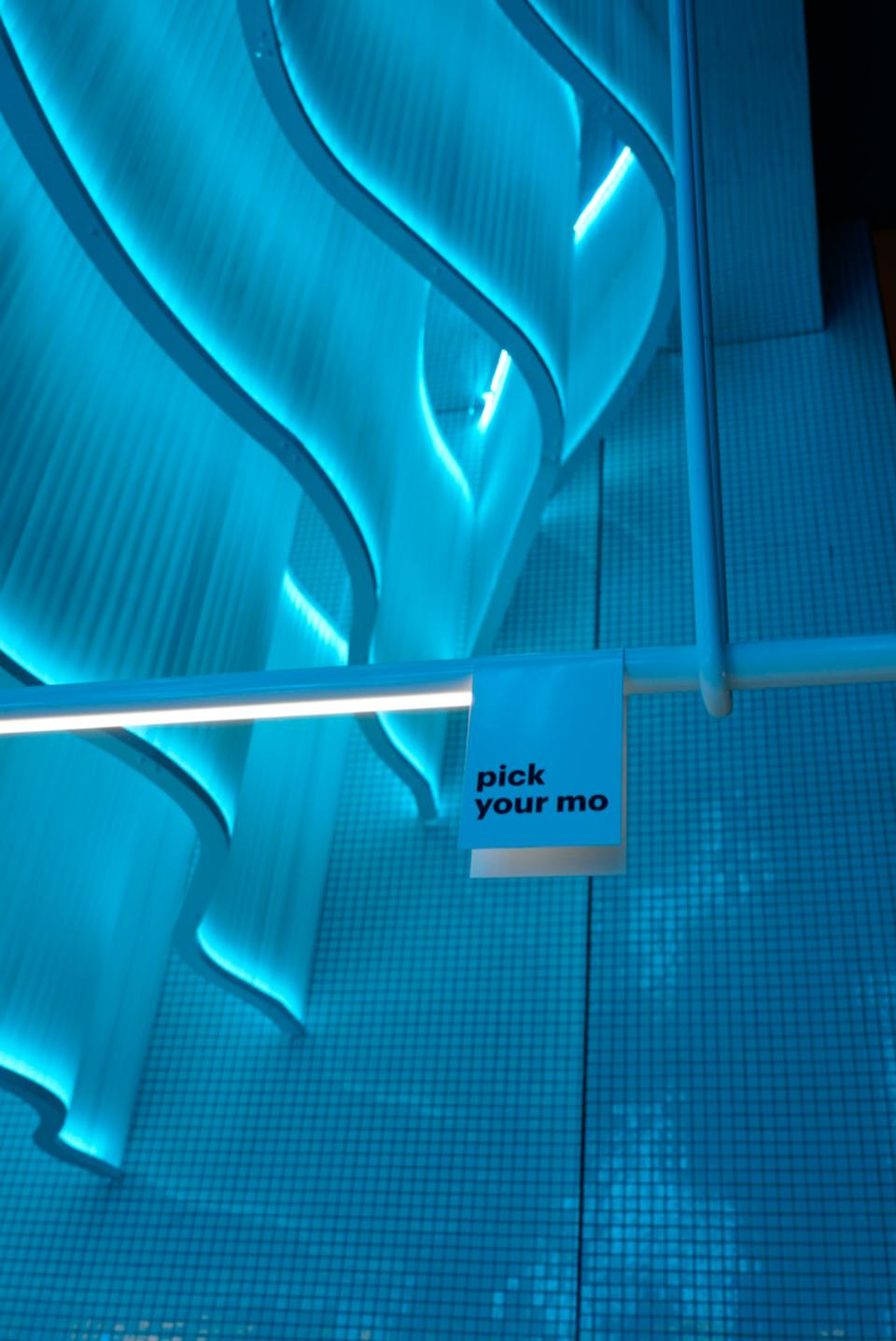 Illuminated interactive sign reading "pick your mo" against a backdrop of blue waves in the MO bakehouse.
