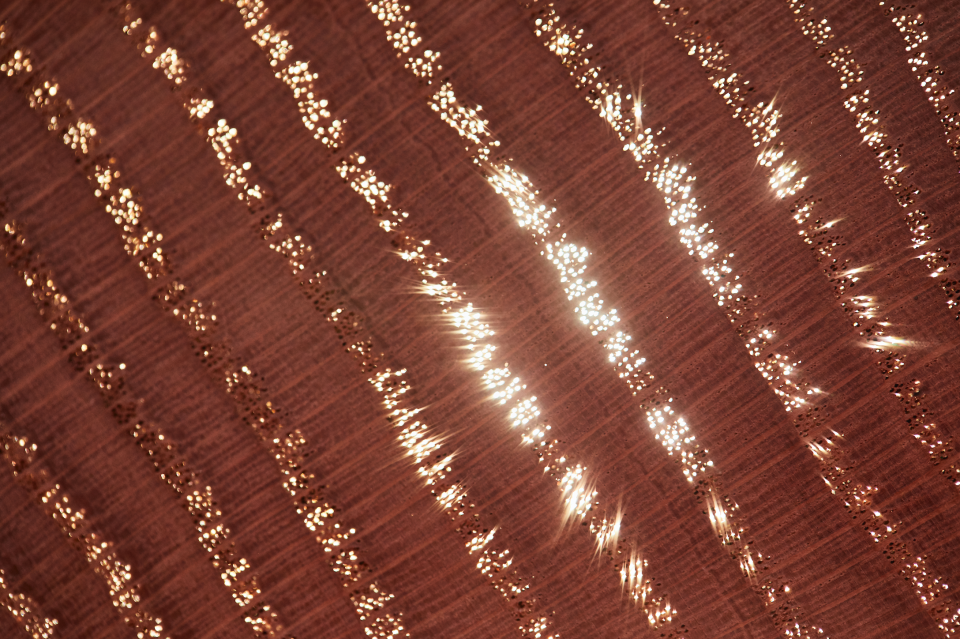 Close-up of a red oak surface showcasing dazzling light reflections and textured patterns, featured in Milan Design Week by Chan + Eayrs.