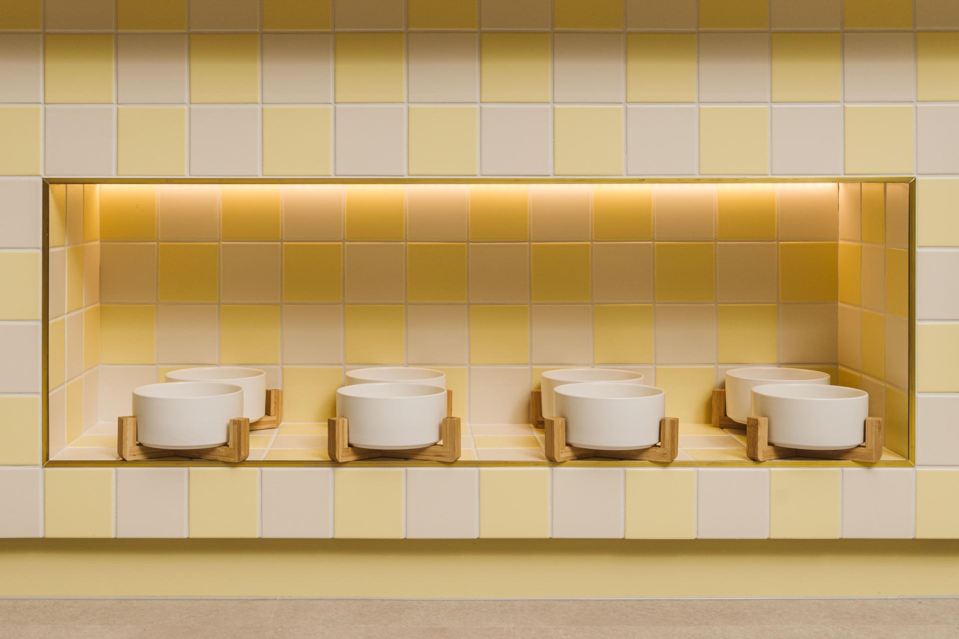Modern pet feeding area with stylish bowls set against a soft yellow tiled background, designed for canine comfort.