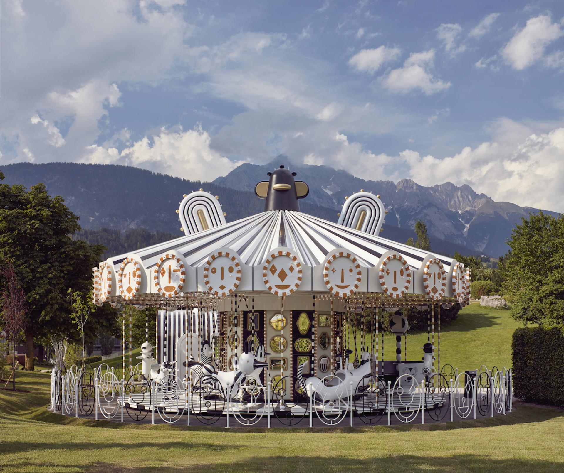 Artistic carousel designed by Jaime Hayon, featuring whimsical horse sculptures against a scenic mountain backdrop.