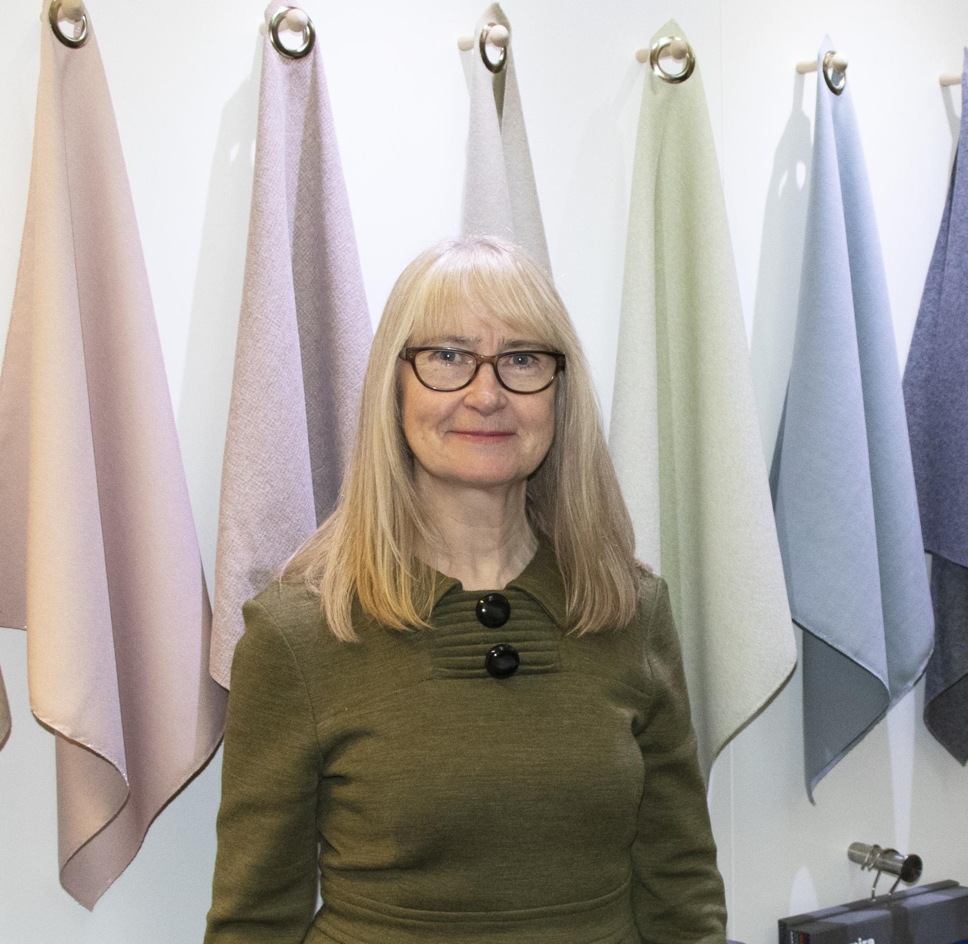 Lynn Kingdon, Head of Contract Design at Camira, stands amidst elegant sustainable fabrics in a design studio.