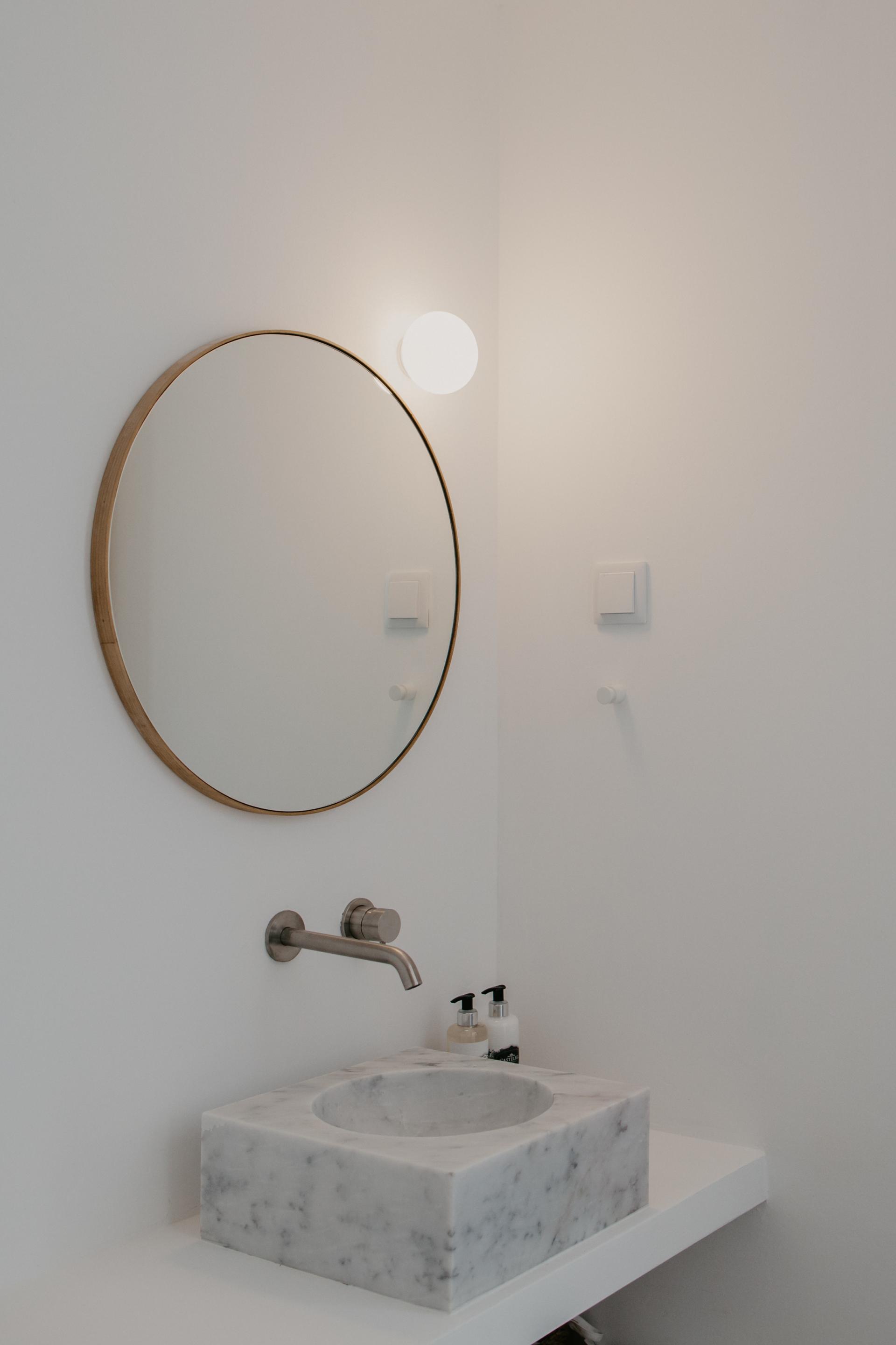 Elegant bathroom design featuring a round mirror, minimalist faucet, and a marble sink, showcasing Quadrodesign's Source collection.