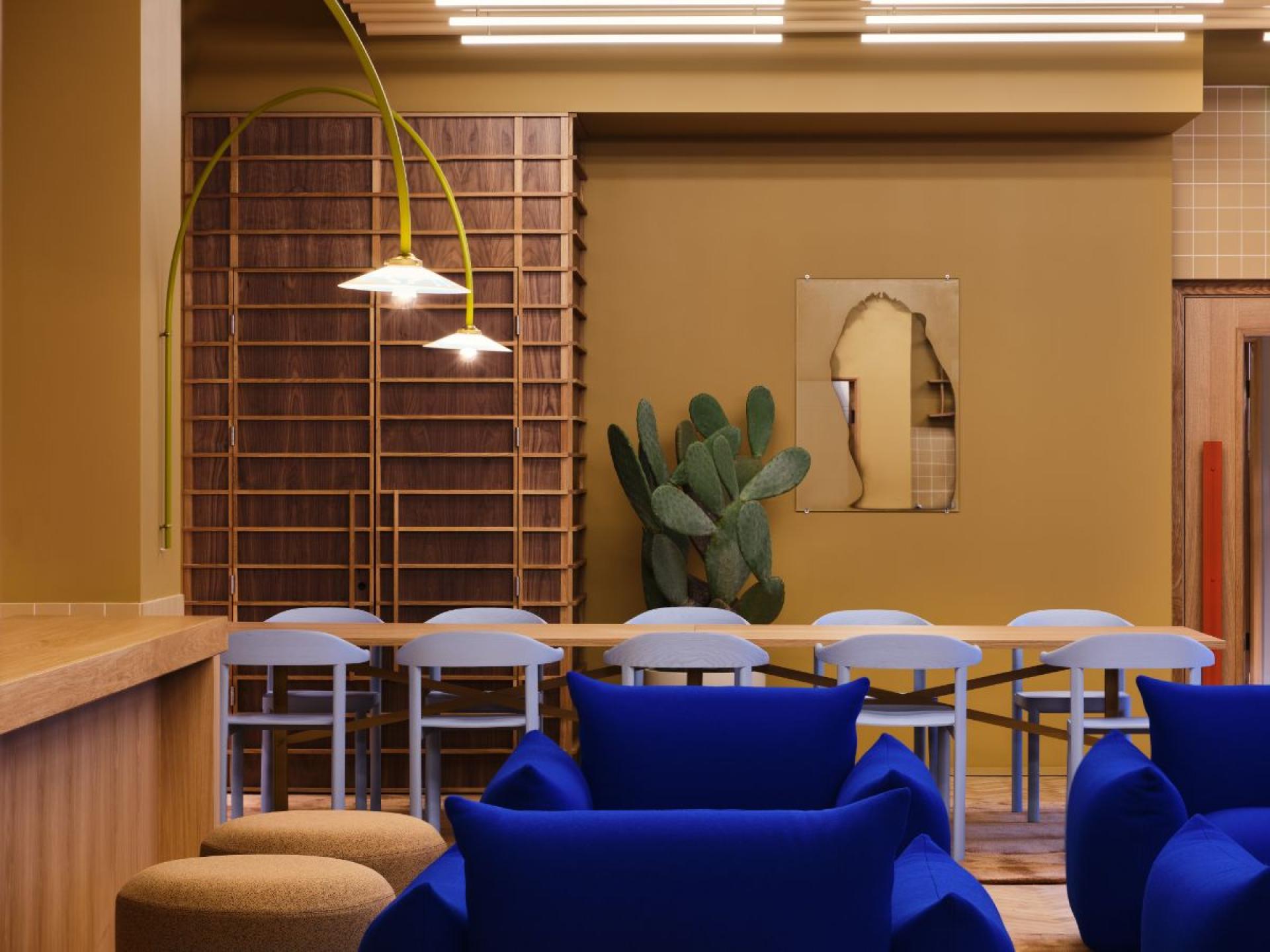 Modern flexible workspace design with vibrant blue seating, wooden dining table, and unique lighting in a stylish London interior.