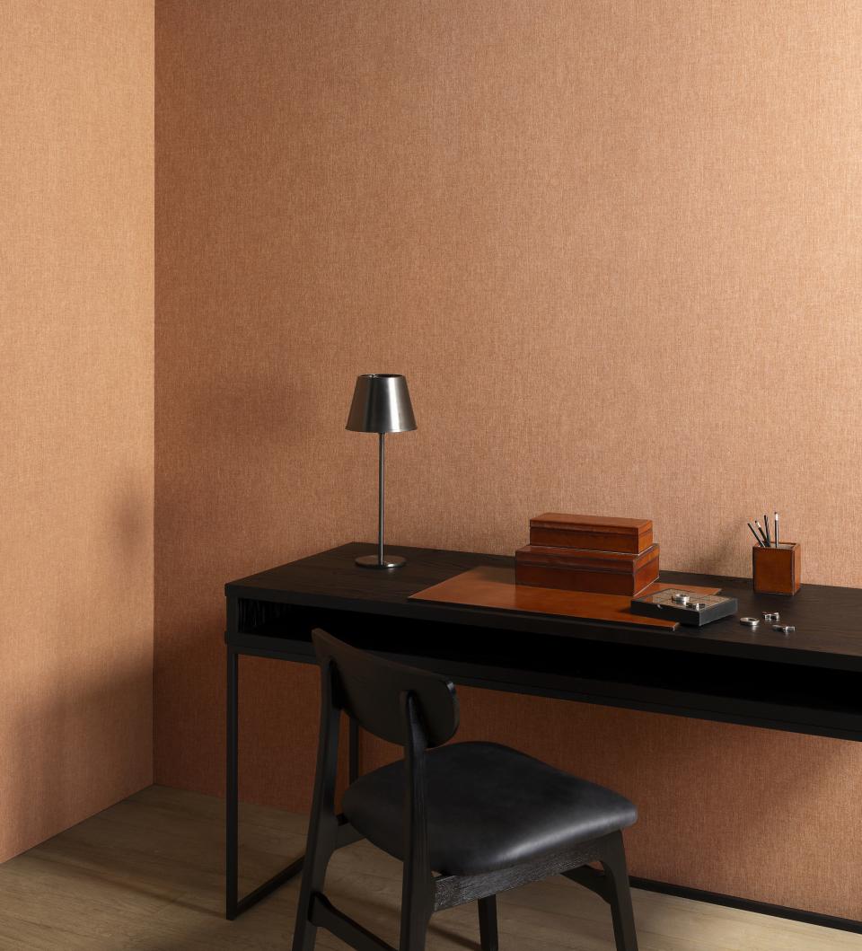 Warm-toned wallcovering decorates a cozy workspace featuring a black desk, lamp, and wooden accessories, showcasing Arte's 2025 collections.