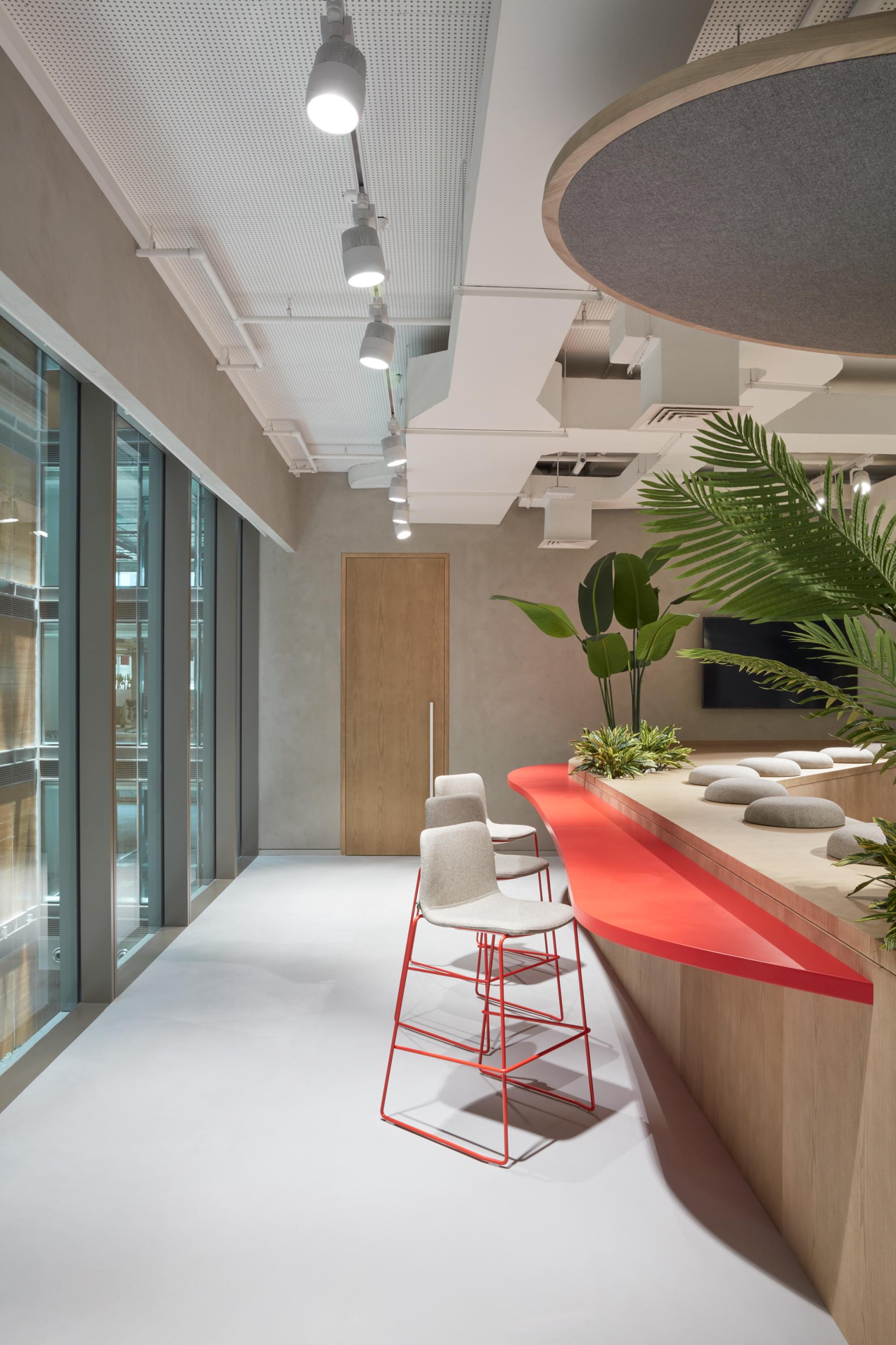 Modern office interior showcasing a sleek red reception desk, minimalist seating, and natural greenery in Takeda's Dubai HQ.