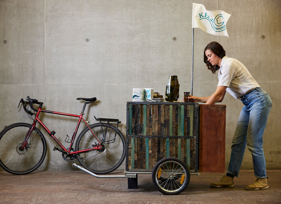 Alex Huller setting up a mobile booth for her kelp farming project, featuring a bicycle and eco-friendly displays.