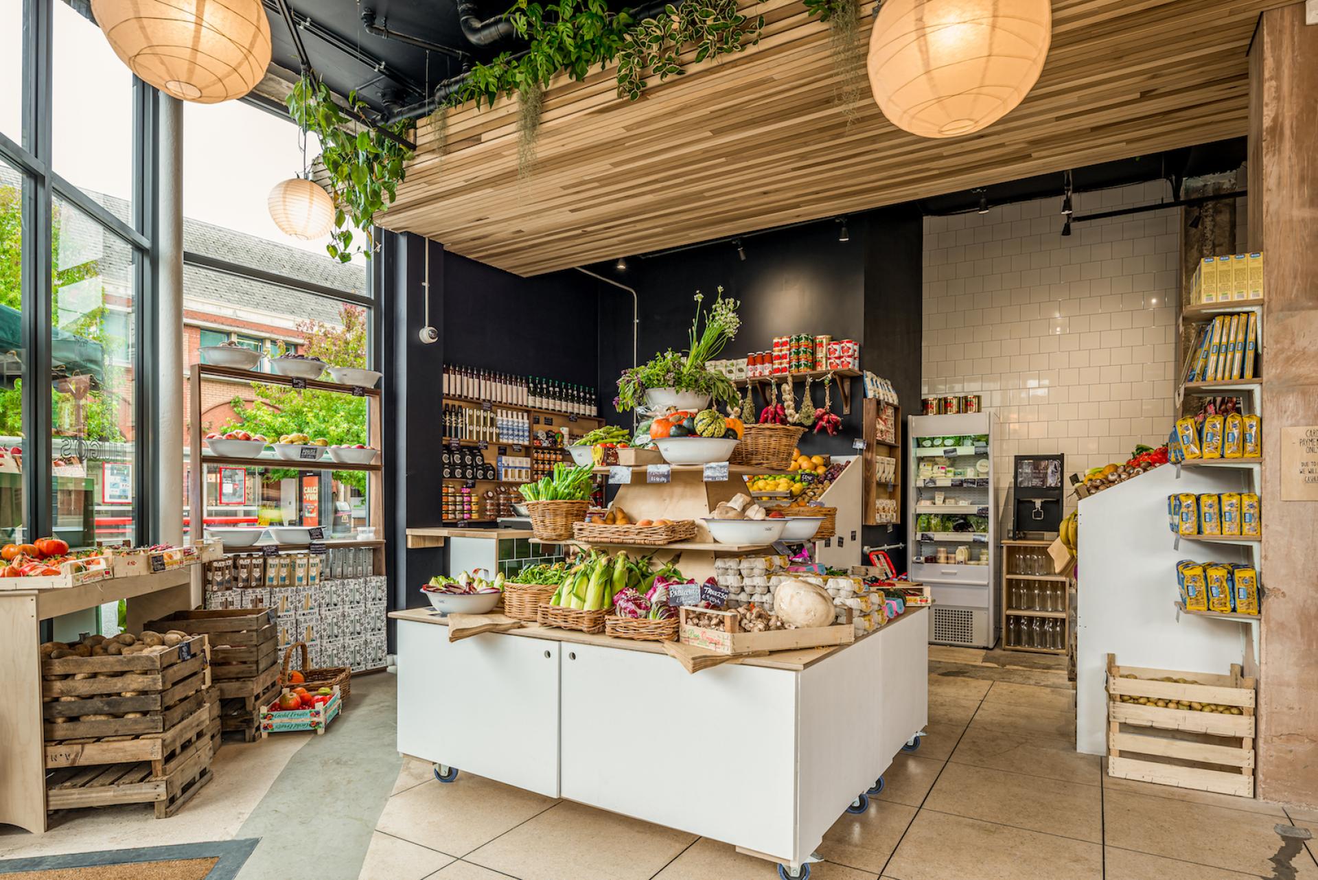 Brightly lit interior of a local grocery store featuring fresh produce, decorative plants, and natural wood accents.