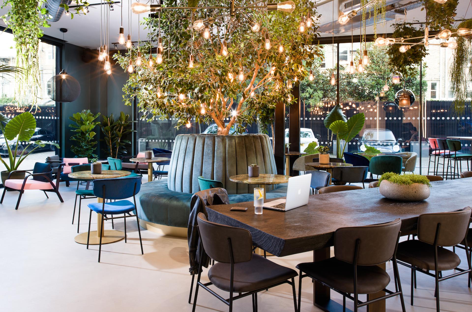 Modern workspace featuring flexible seating, greenery, and stylish lighting, promoting an innovative approach to workplace design.