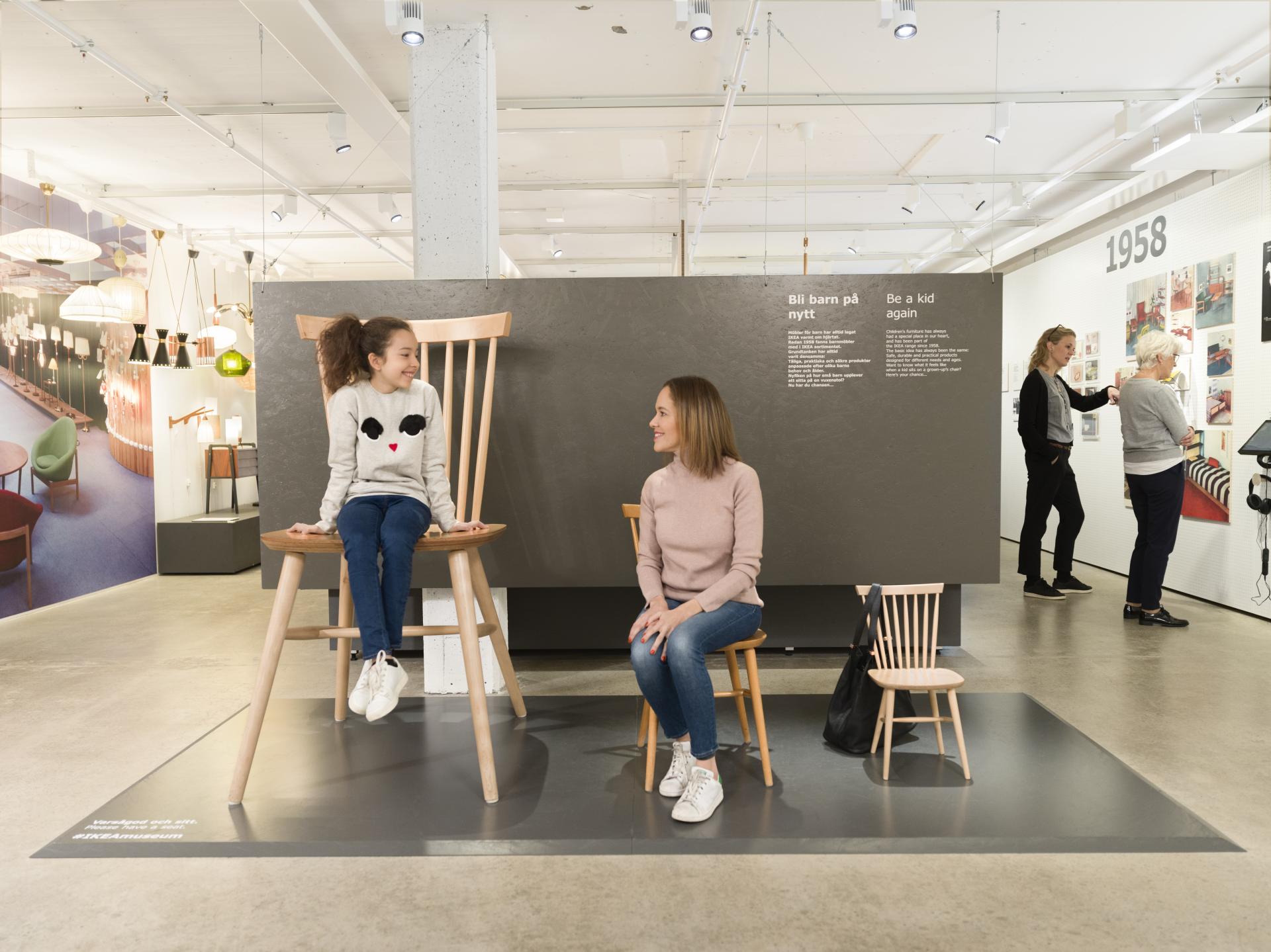 Young girl and woman sit on oversized and regular chairs in the IKEA Museum, highlighting playful design and family experiences.