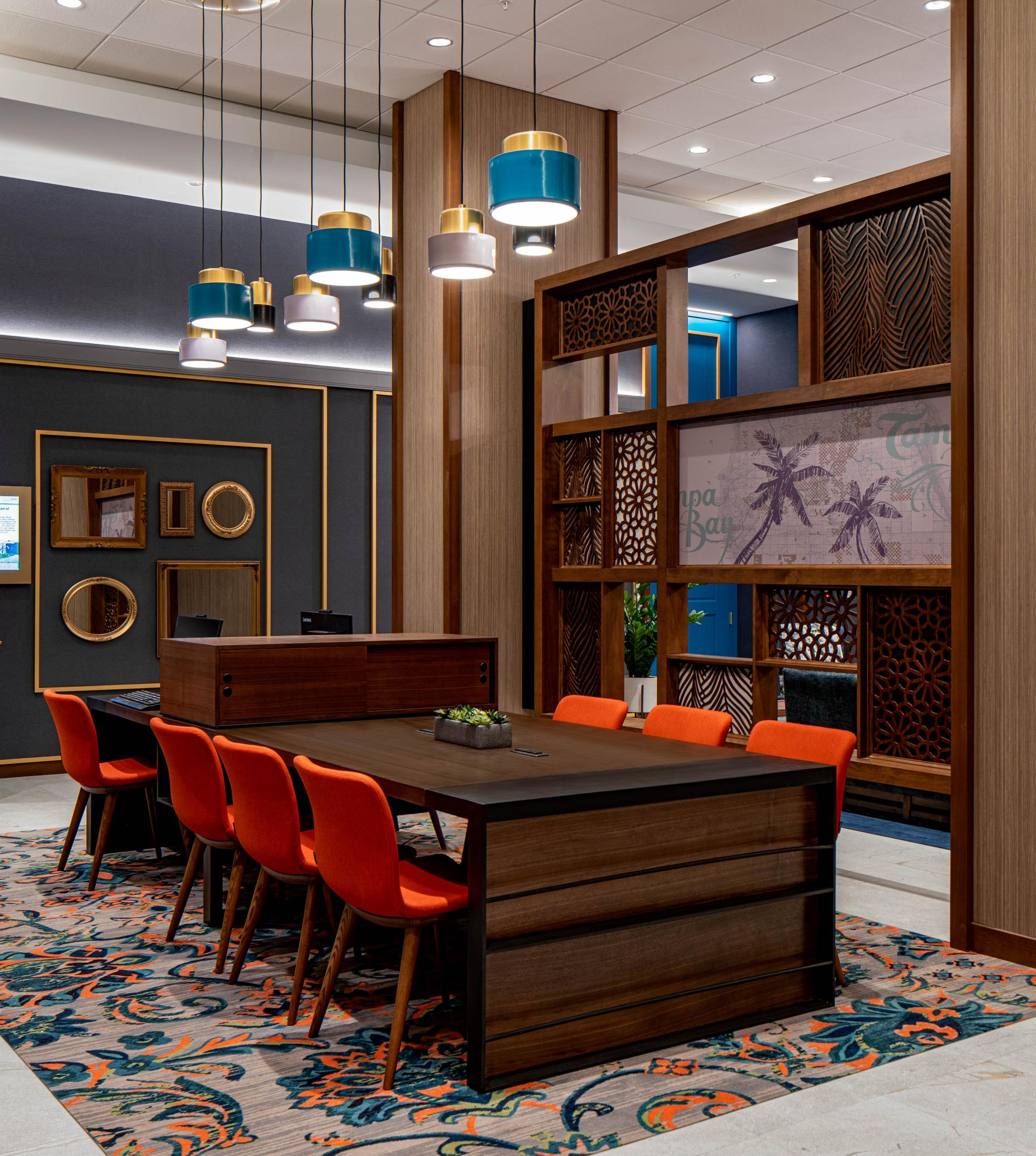Modern hotel lobby with vibrant orange chairs, geometric patterns, and stylish pendant lights at Hyatt House, Tampa.